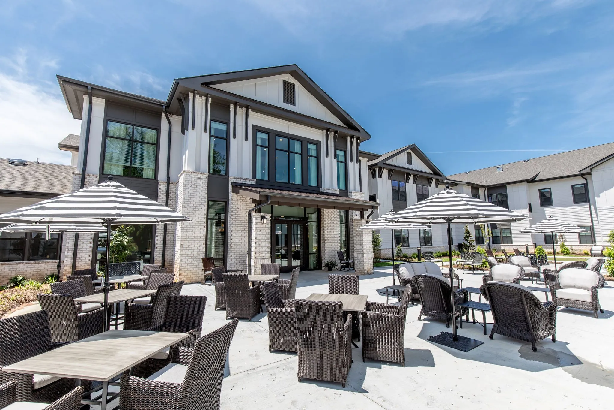 Senior living courtyard with striped umbrellas over woven patio seating in front of the community