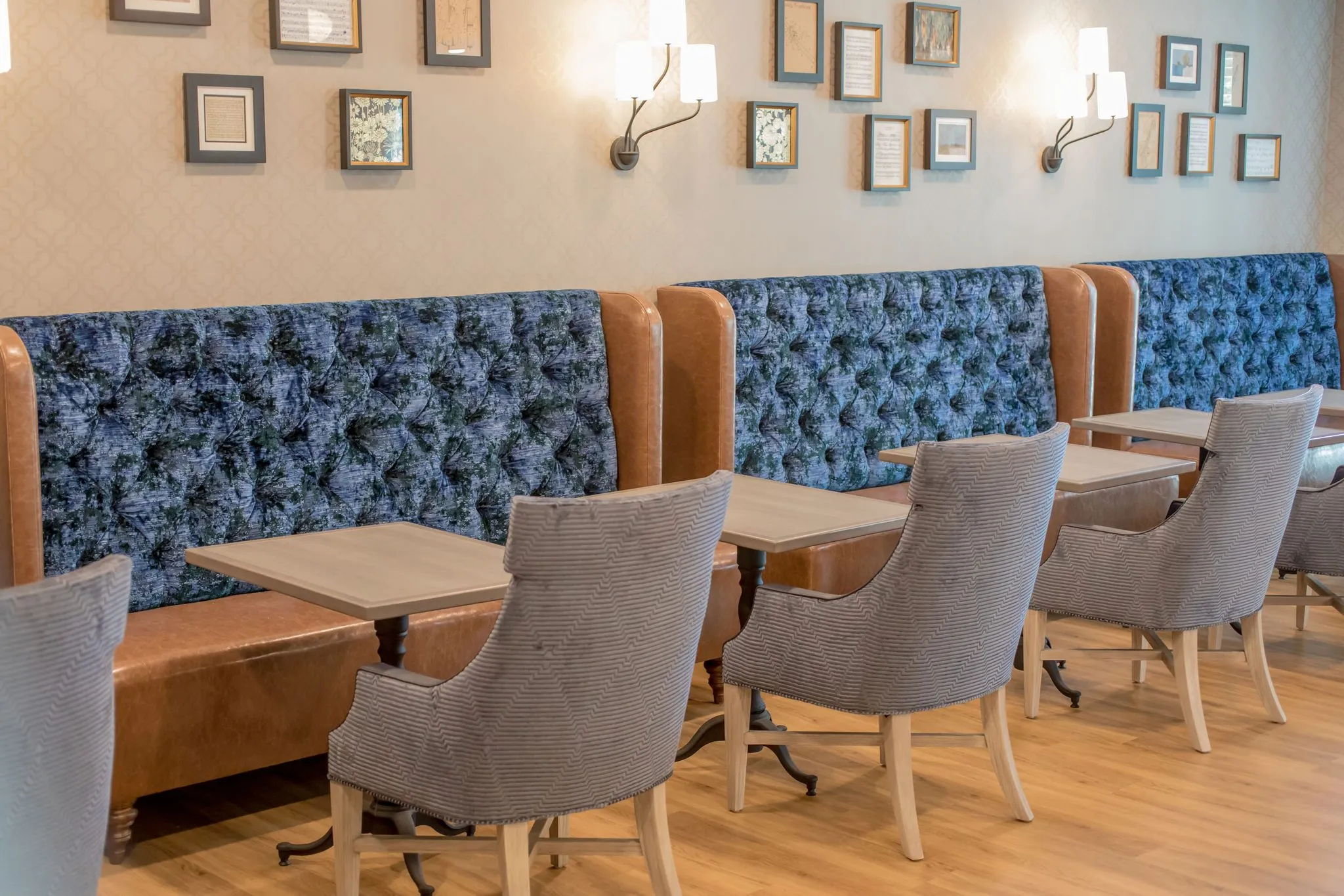 Senior living dining banquette of blue floral tufted seating with tan leather ends below a gallery of framed prints