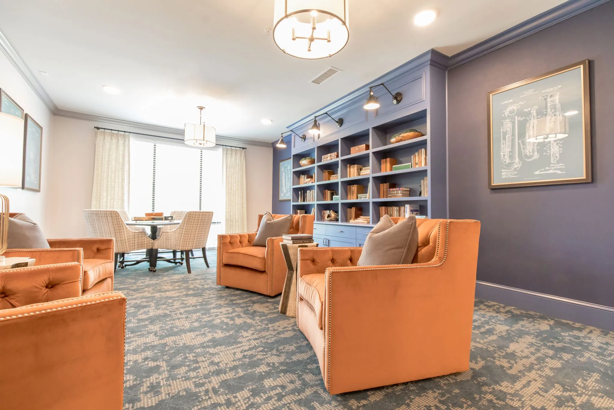Senior living library lounge with rust tufted armchairs facing blue built-in bookcases on a purple wall