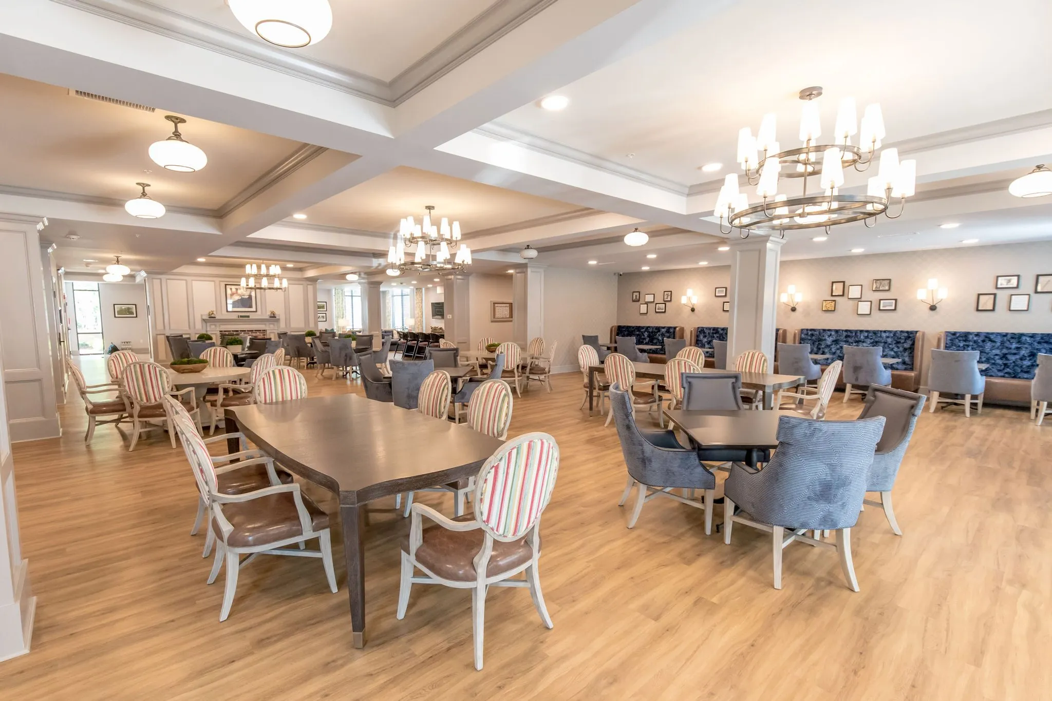 Senior living main dining room with chandeliers under a coffered ceiling above striped and blue velvet chairs