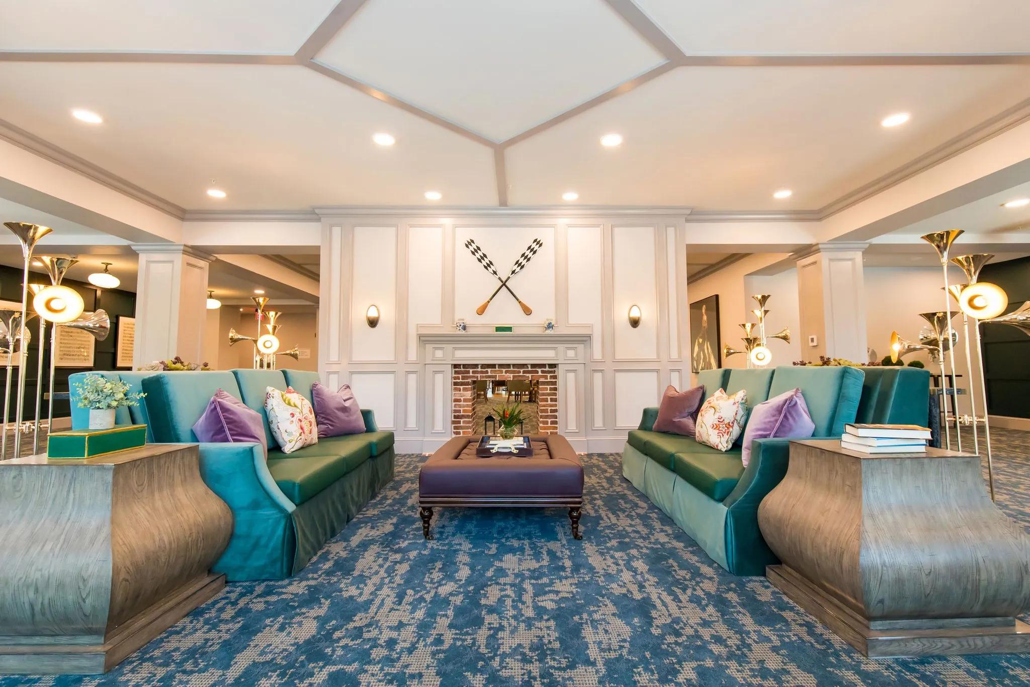 Senior living music room with teal high back sofas around a purple ottoman, crossed oars above a brick fireplace