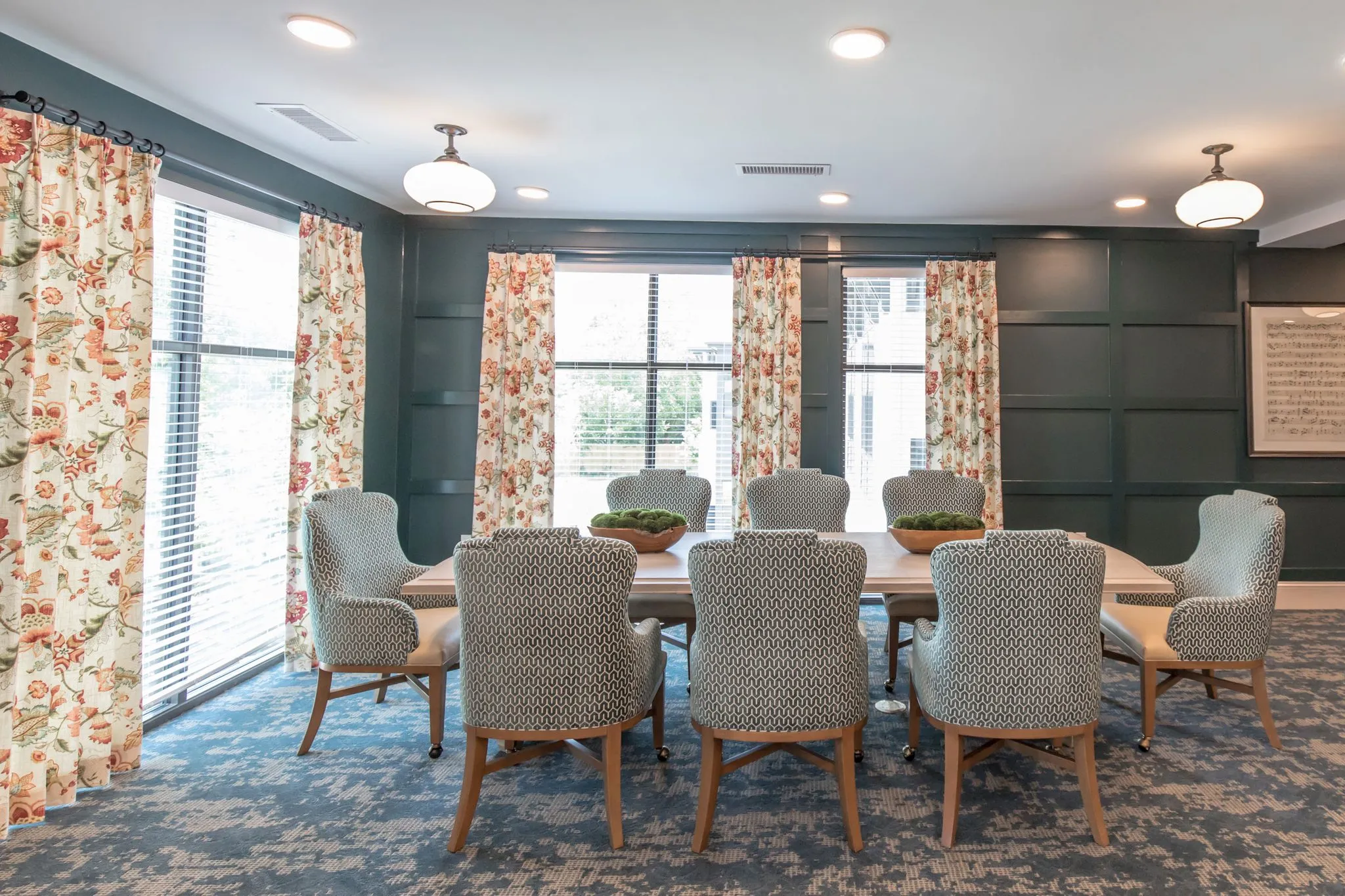 Senior living private dining room with patterned chairs at a long table against dark green panelling and floral drapery