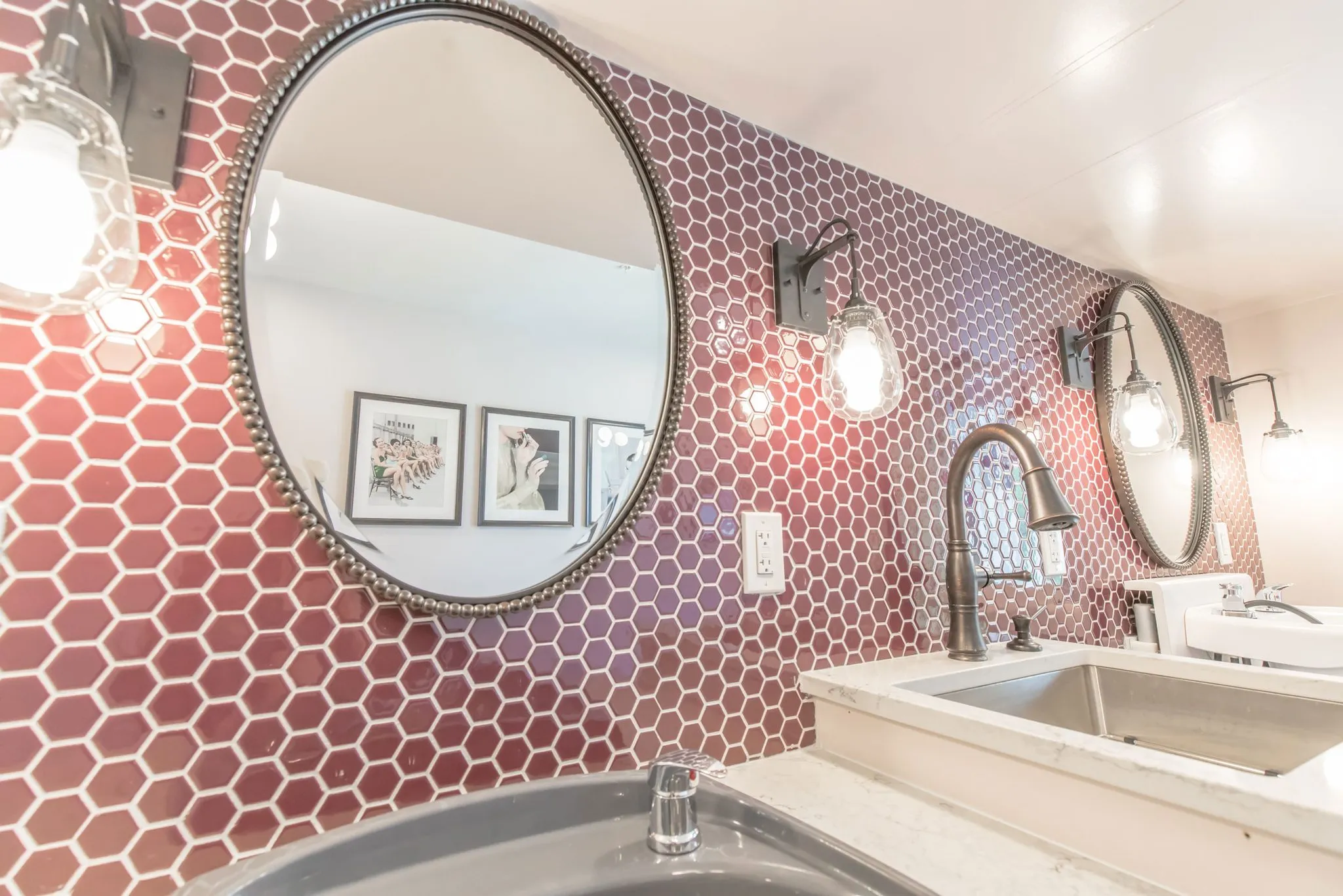 Senior living salon with round mirrors and sconces on a wall of raspberry hexagon tile
