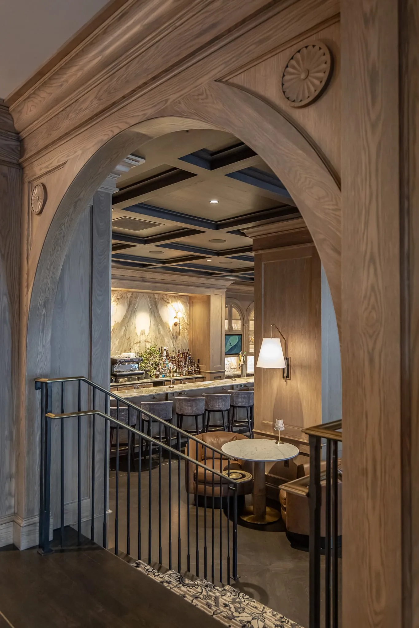 Arched oak doorway opening onto a dining room and bar with pendant lamps, an iron railing and a round marble table