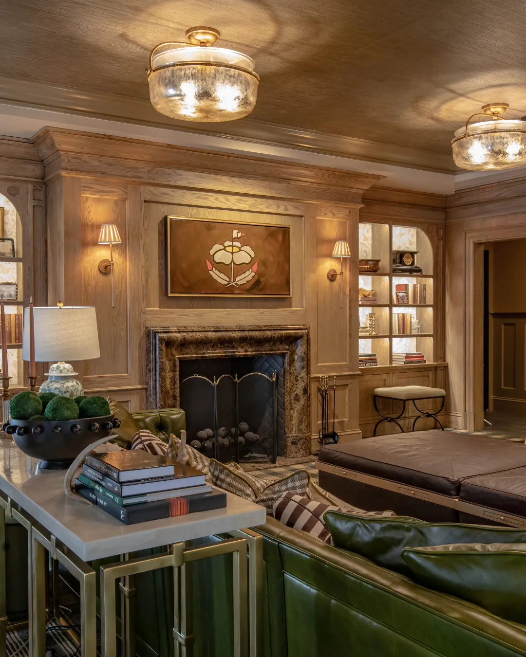 Private club lounge with oak panelling, a marble fireplace, lit glass-front bookcases, a green leather sofa and a crest painting
