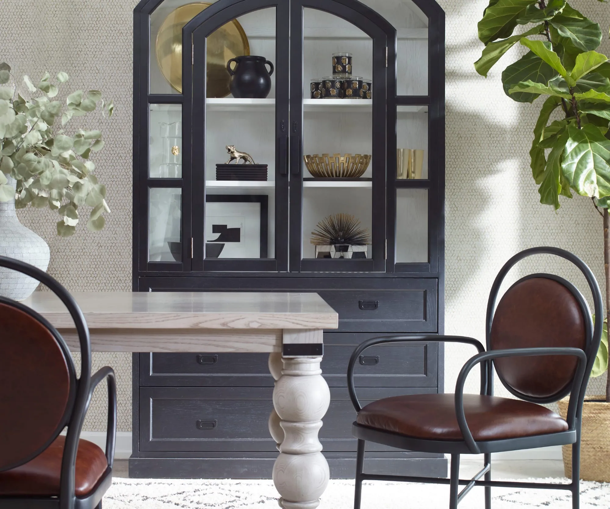 Dining vignette with a black arched glass-front cabinet, a white turned-leg table, black bentwood chairs with leather seats and a potted fig