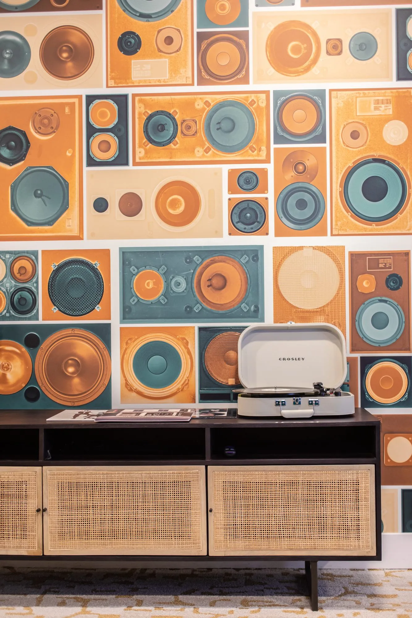Student housing interior detail: record player on a rattan fronted console against wallpaper printed with retro speakers