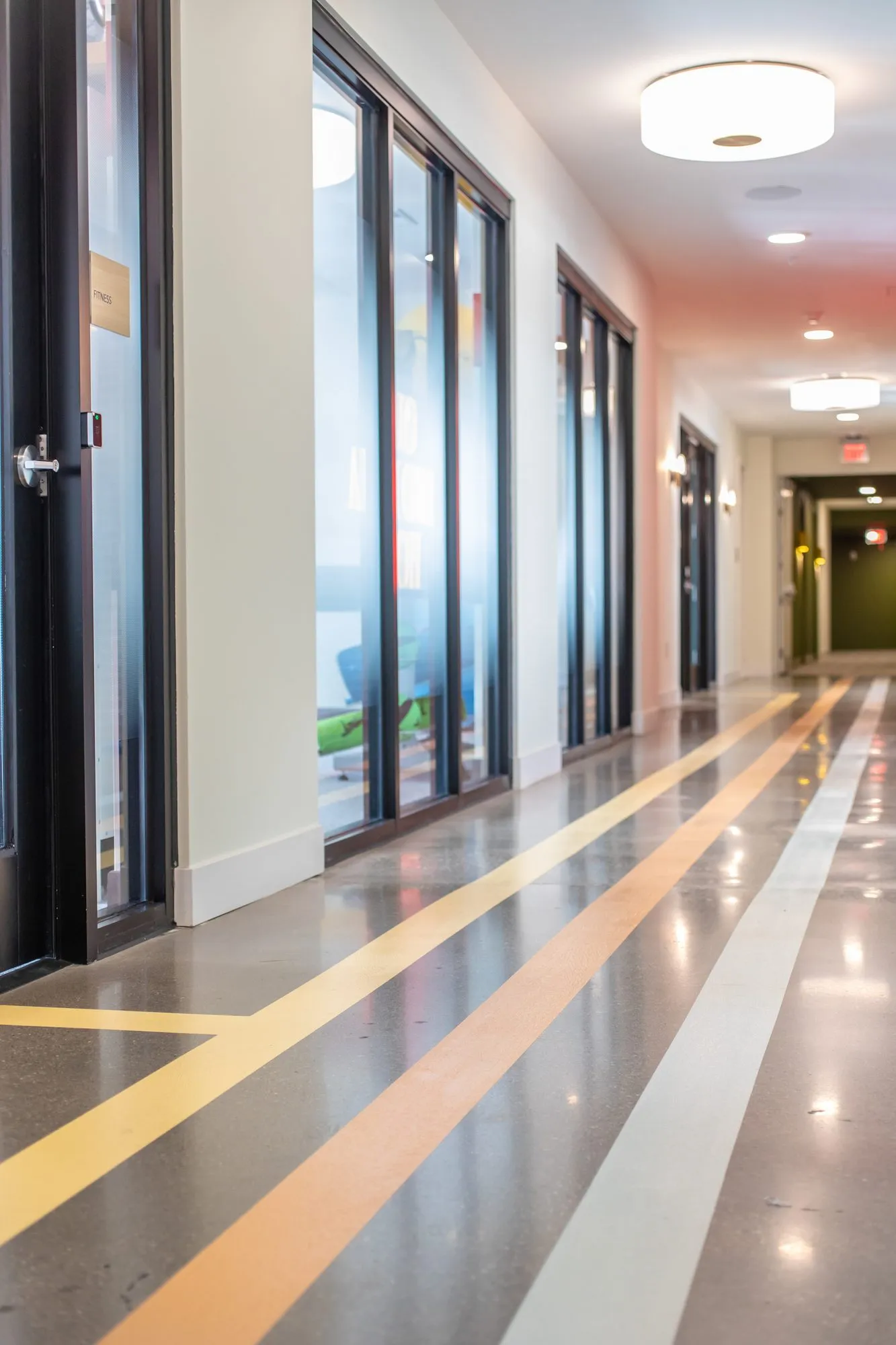 Student housing amenity corridor, polished concrete striped yellow, orange and white past black framed glass rooms