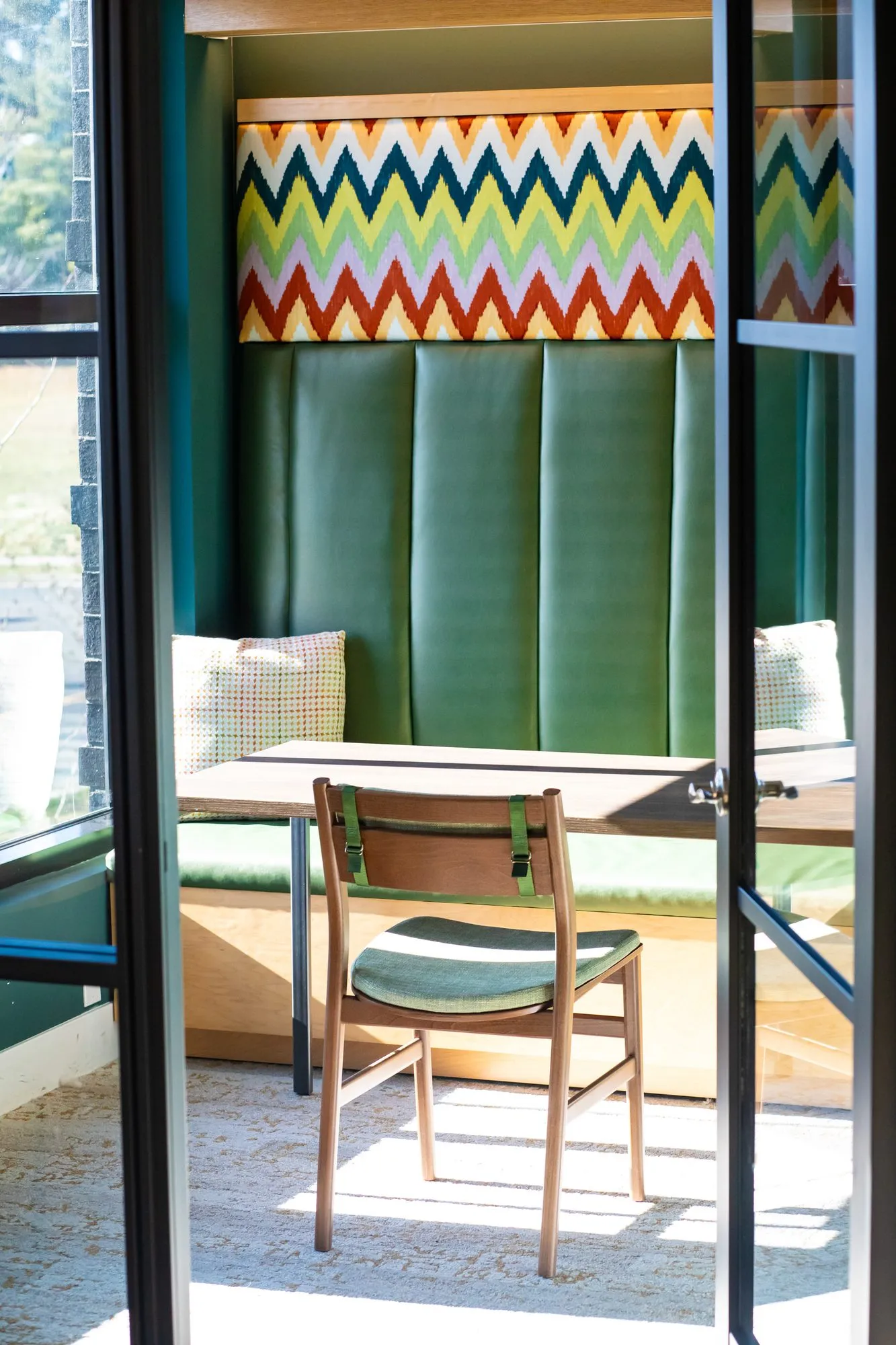 Student housing amenity study booth with a green channel tufted banquette and chevron panel, seen through glass doors