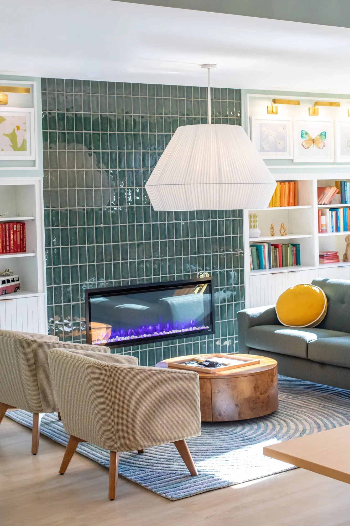 Student housing interior detail: green tiled fireplace with a linear electric fire between white bookshelves, pleated pendant