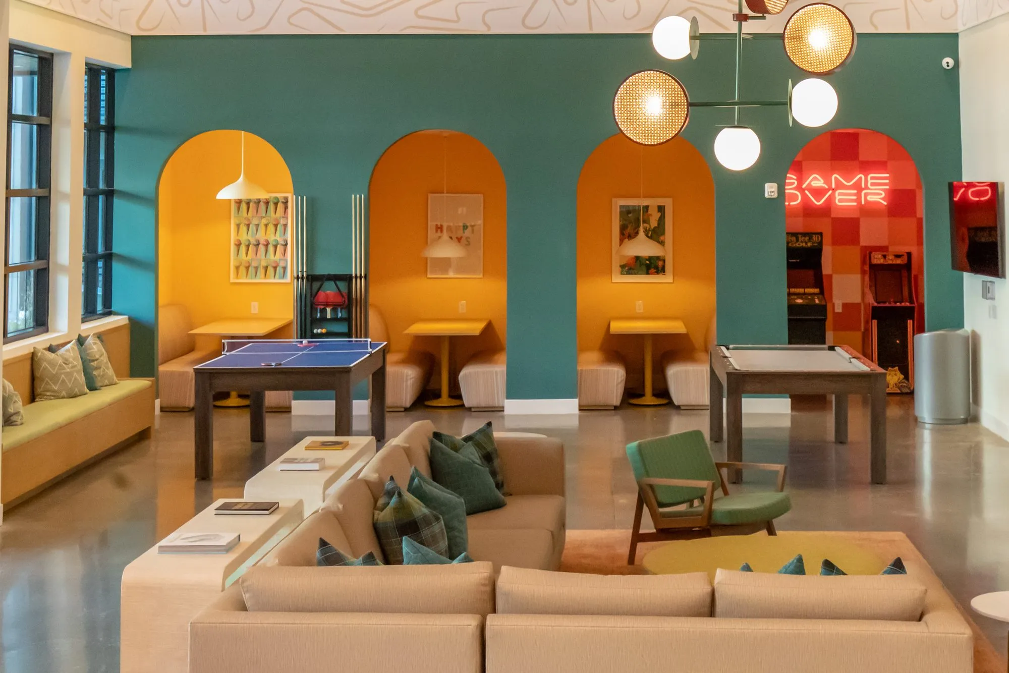 Student housing amenity game room with a ping pong table before orange arched booths on a teal wall, sectional in front