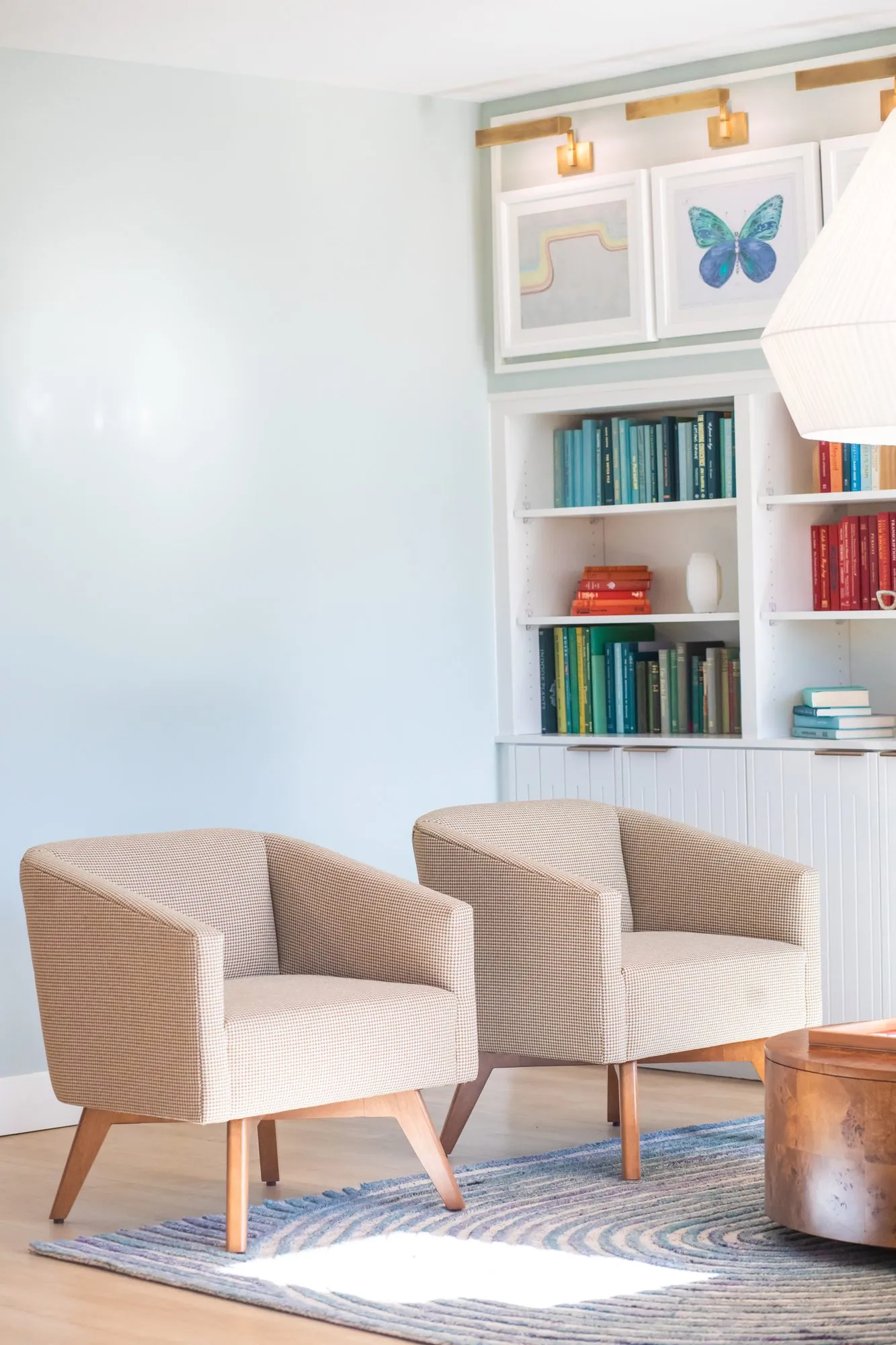 Student housing interior detail: two oatmeal armchairs on a swirl rug before white shelving with colour-sorted books