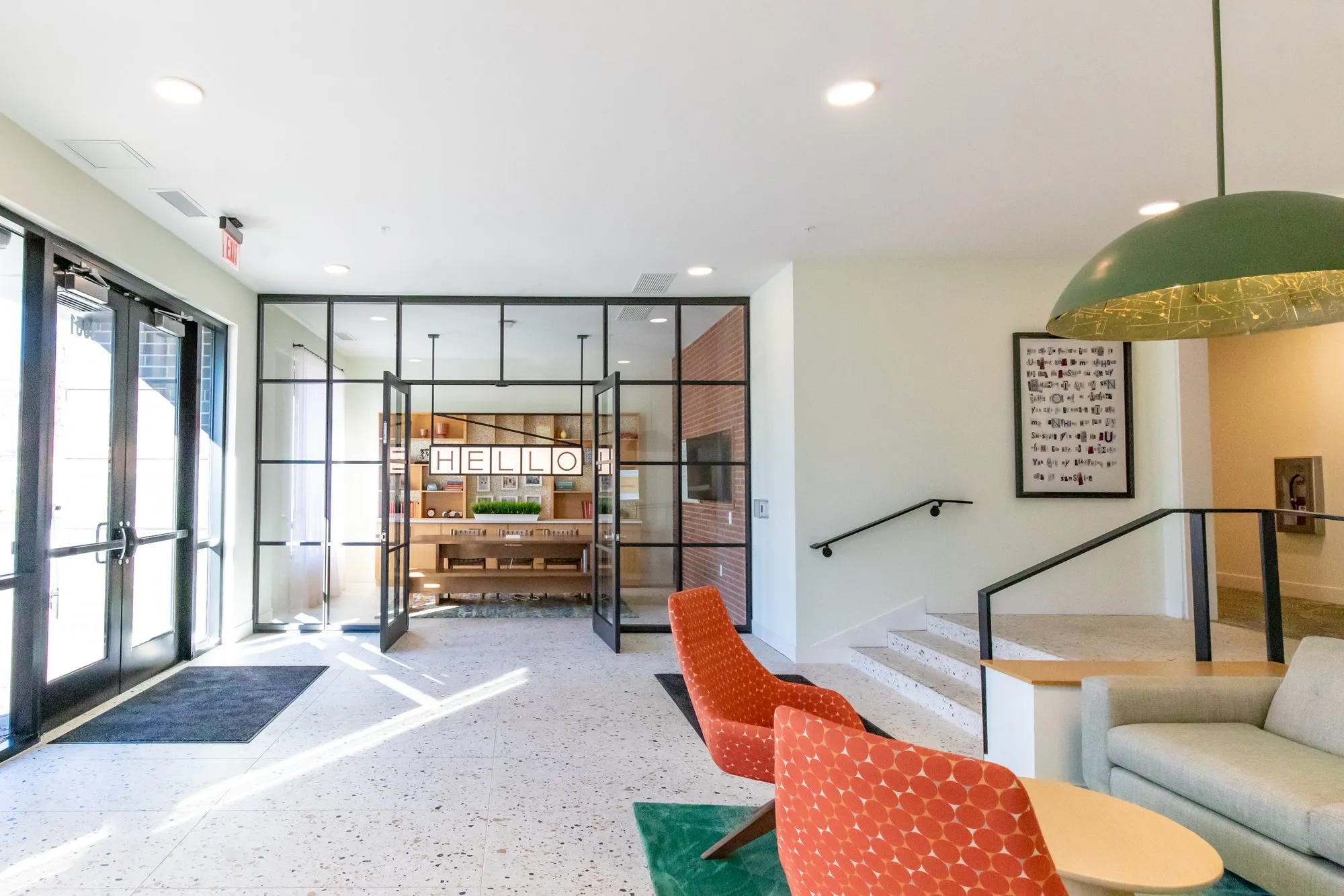 Student housing amenity entry with a terrazzo floor, orange chairs and a green dome pendant looking to glass doors