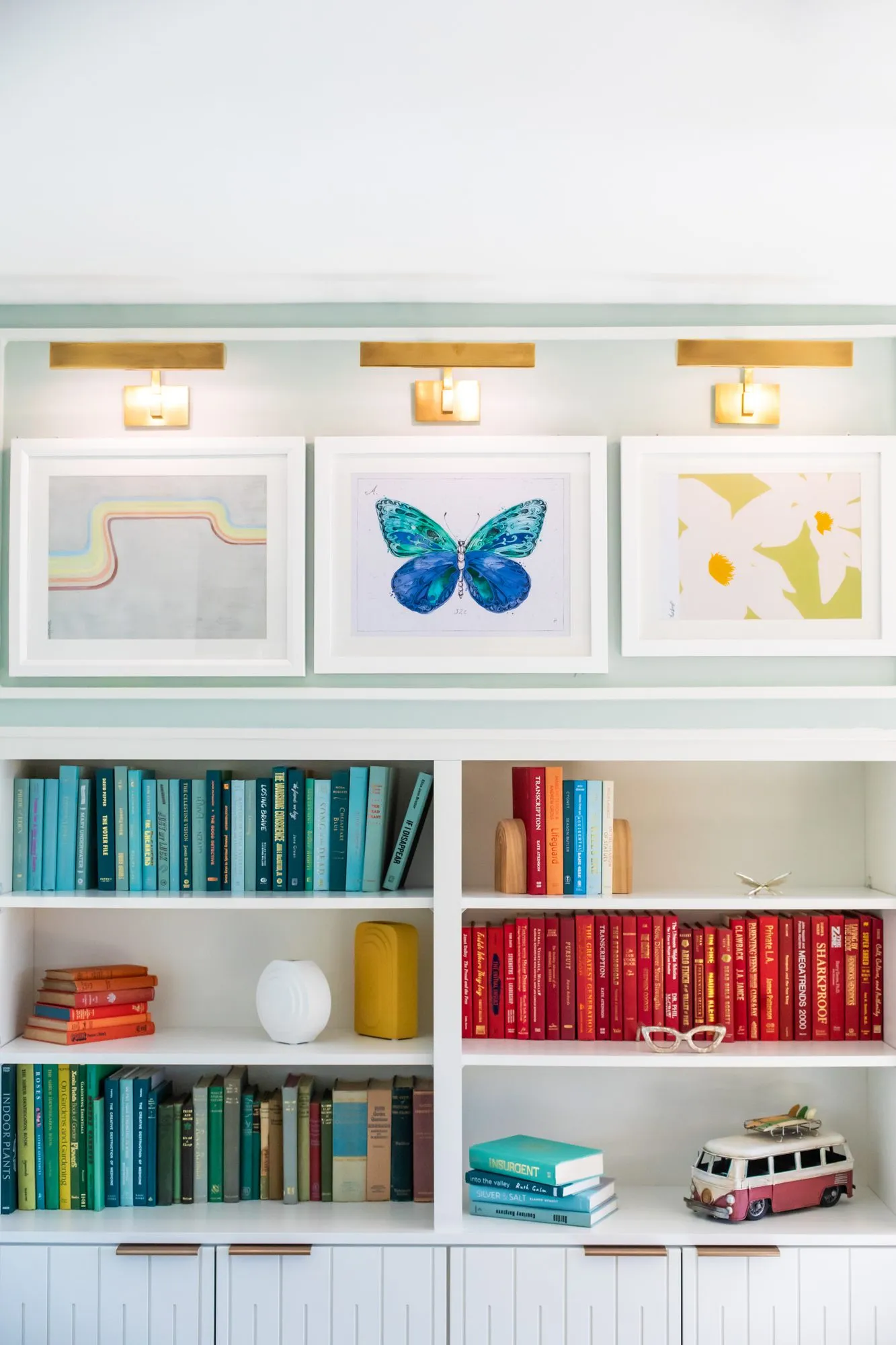 Student housing interior detail: white shelving of blue, red and green books and a toy camper van below three framed prints