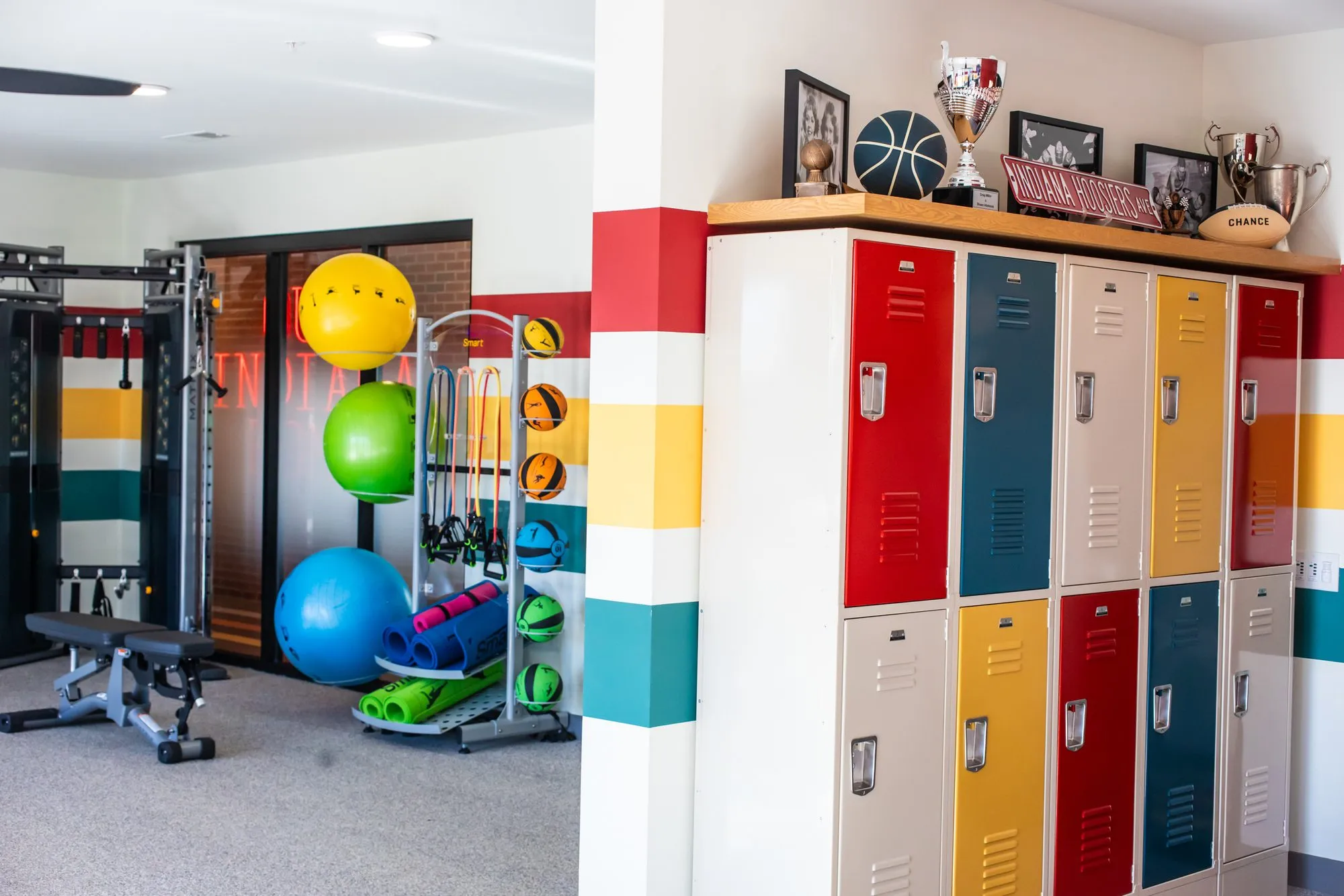 Student housing amenity weight area with exercise balls and a functional trainer beside colourful lockers and striped walls