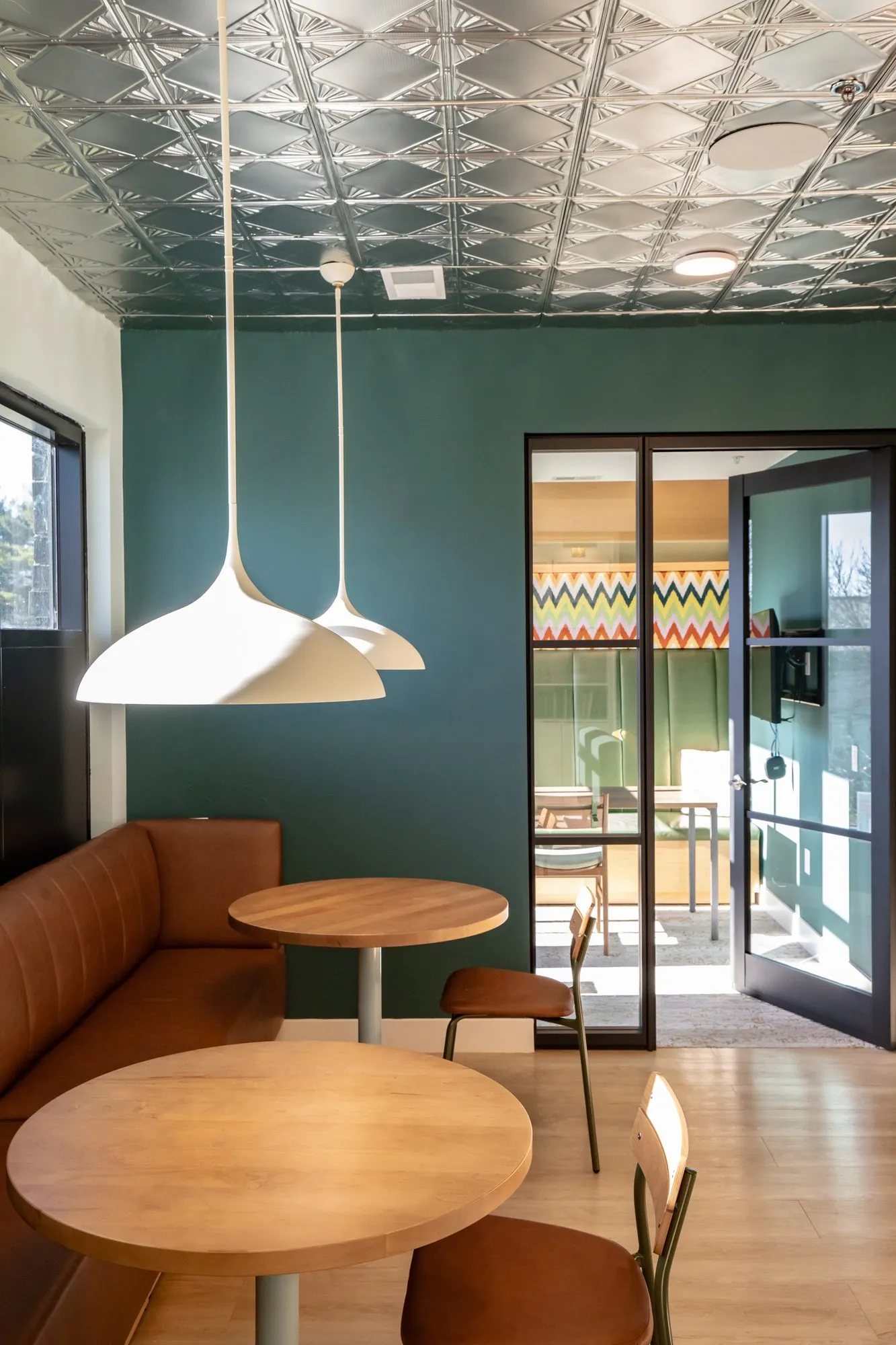 Student housing amenity cafe with a cognac leather banquette, wood tables and white pendants under a pressed tin ceiling