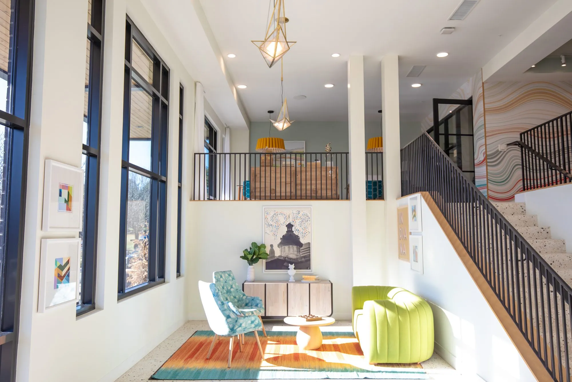 Student housing amenity double-height lounge with a lime green sofa and floral chairs on a striped rug, stair and mural