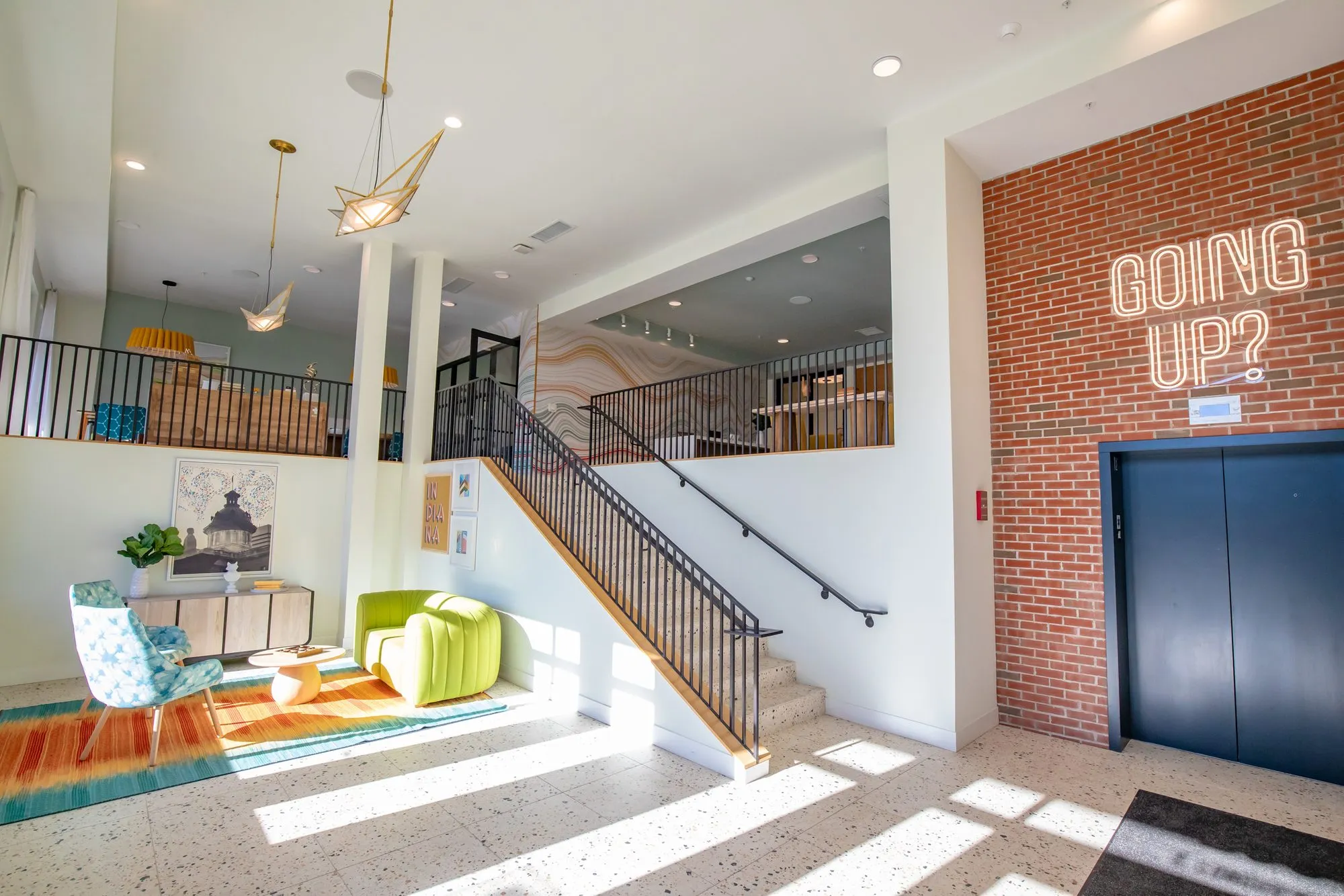 Student housing amenity lobby: terrazzo floor and a stair to the mezzanine beside the elevator and a Going Up? neon