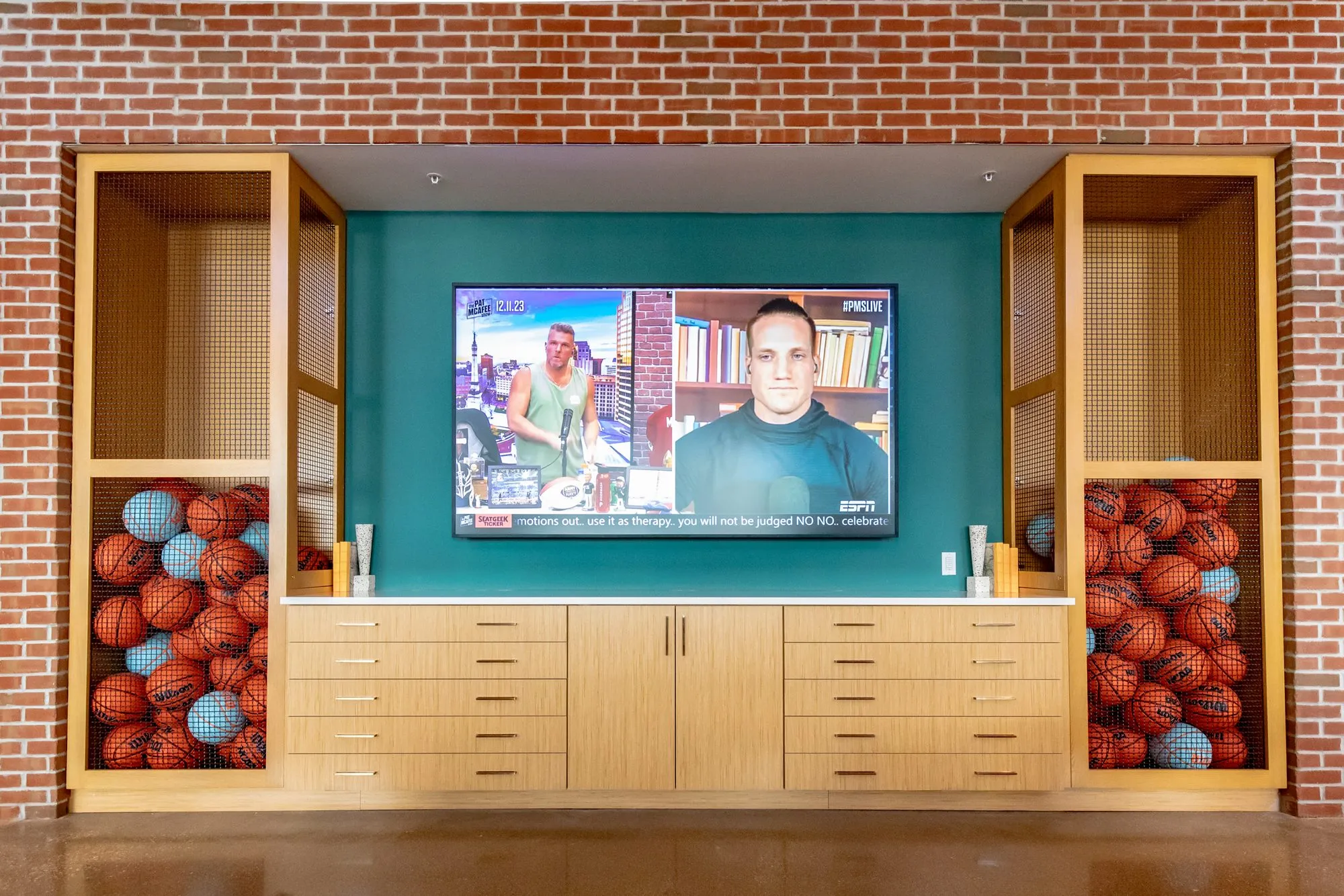 Student housing interior detail: wall screen on teal above wood drawers, flanked by cubbies of basketballs against brick