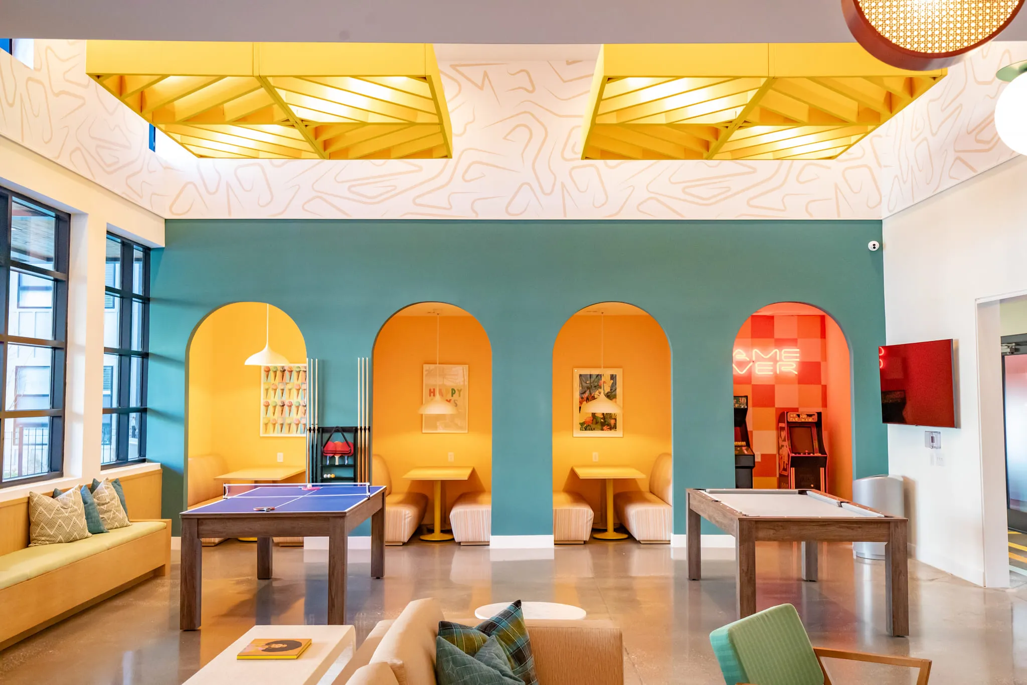 Student housing amenity game room with orange arched booths and a red Game Over neon behind ping pong and shuffleboard