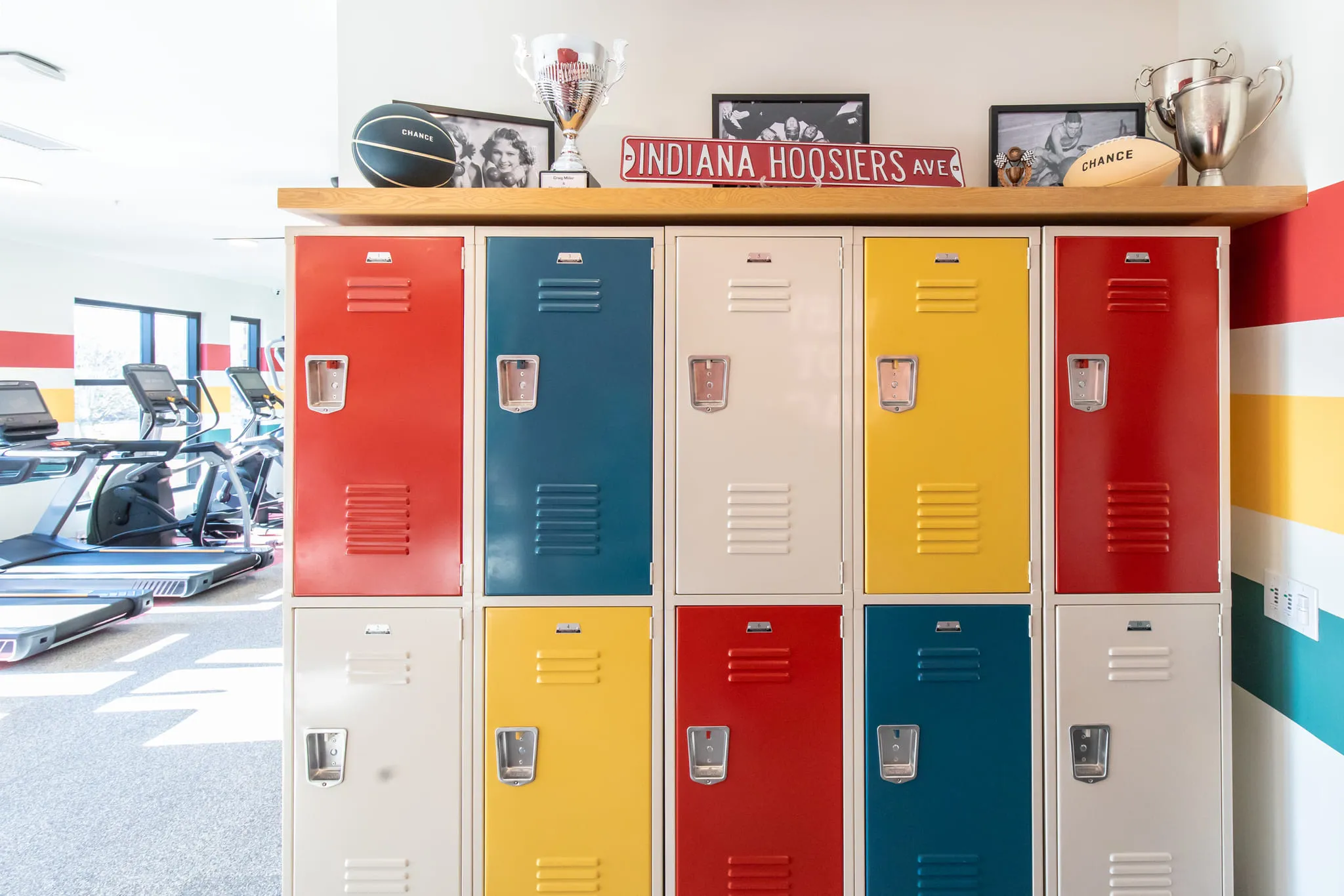 Student housing amenity gym lockers in red, blue and yellow topped with trophies and Indiana sports memorabilia