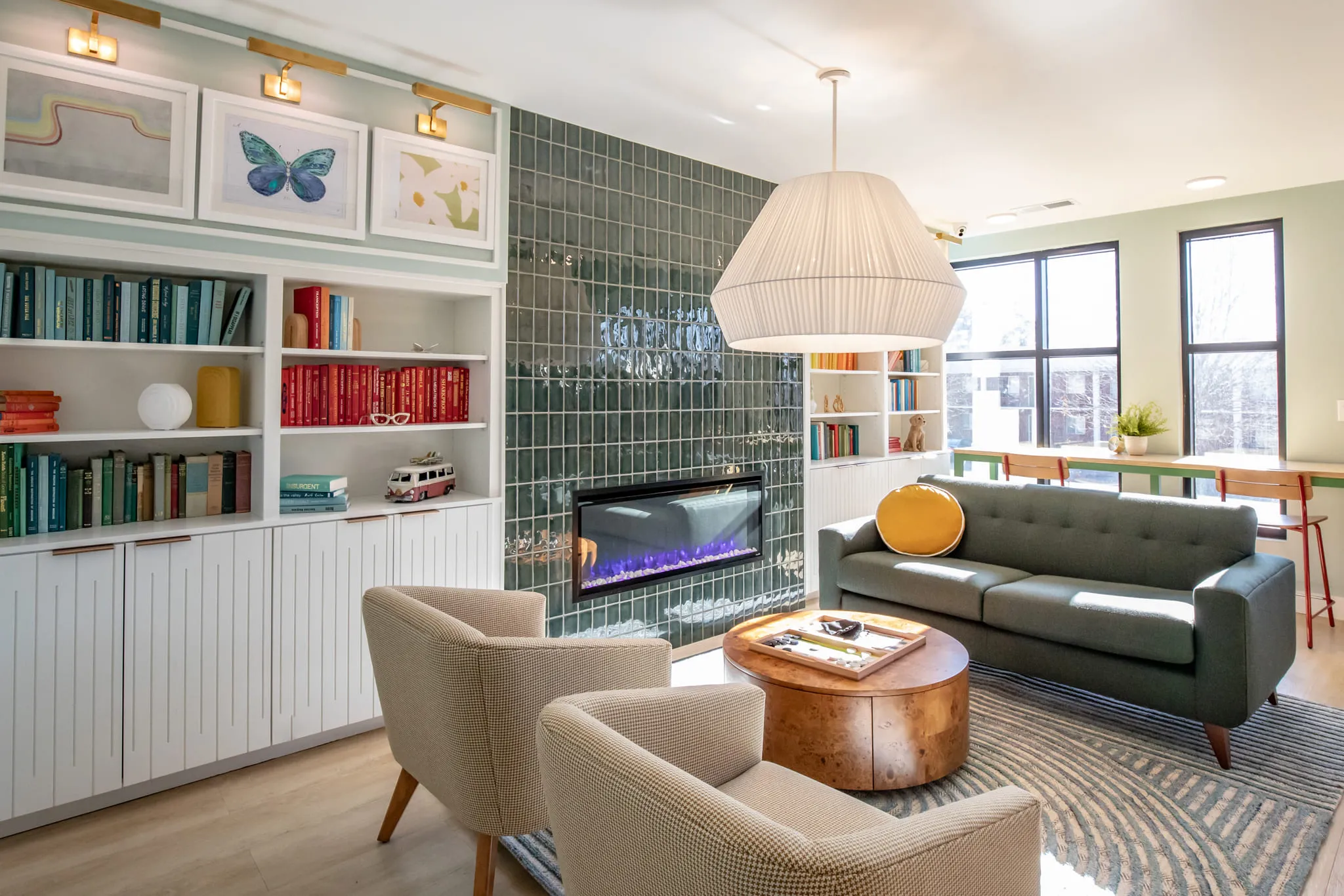 Student housing amenity library lounge with color-sorted books on white shelving by a green tiled fireplace and green sofa