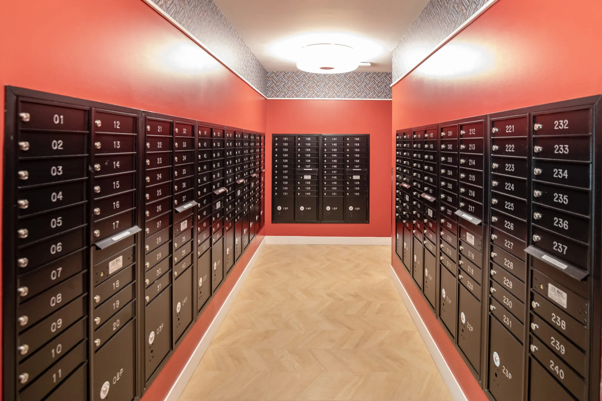 Student housing amenity mail room with rows of black mailboxes running the length of a coral painted corridor
