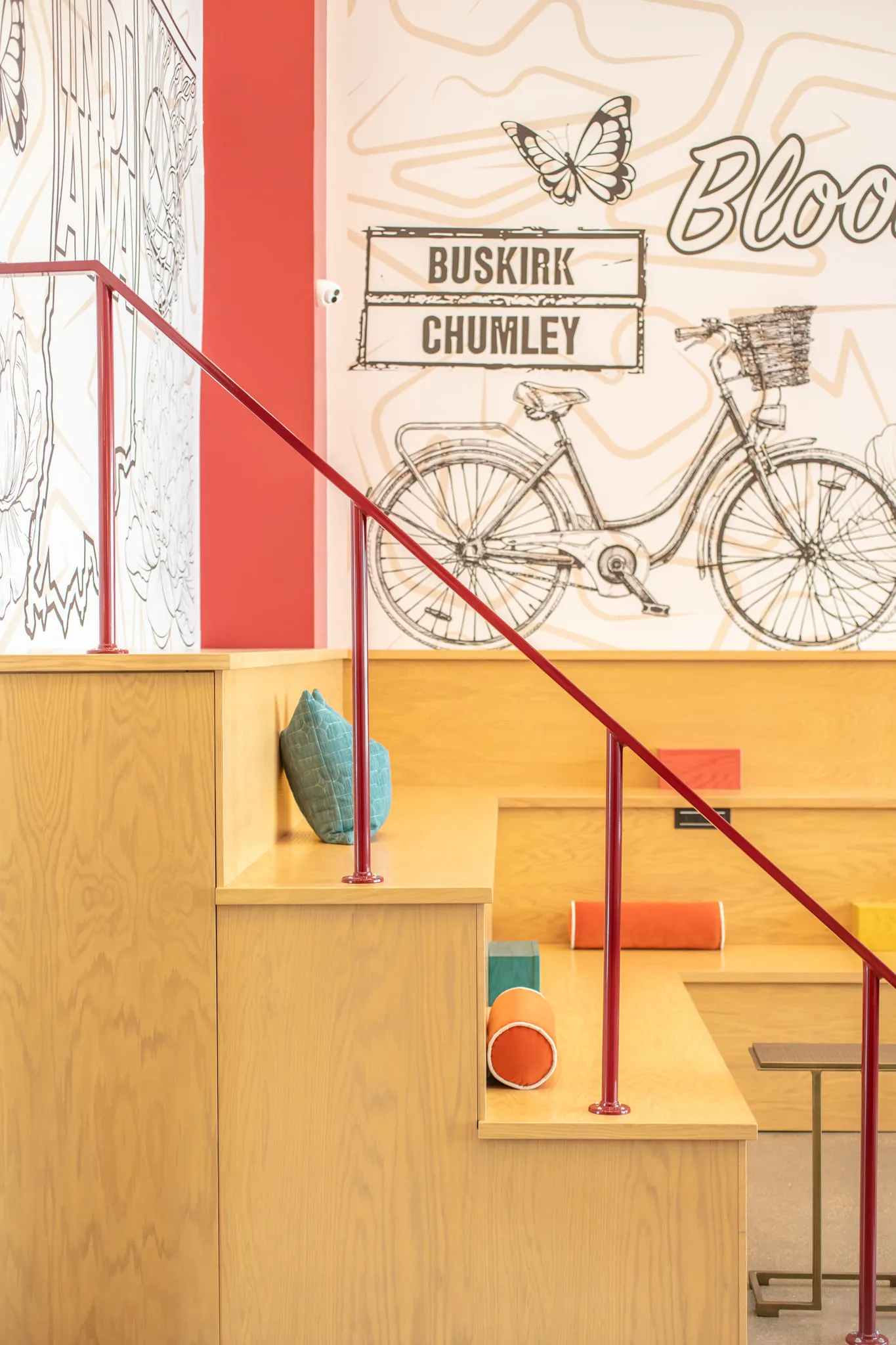 Student housing amenity plywood bleachers: stepped seating and a red handrail below the line drawn bicycle mural