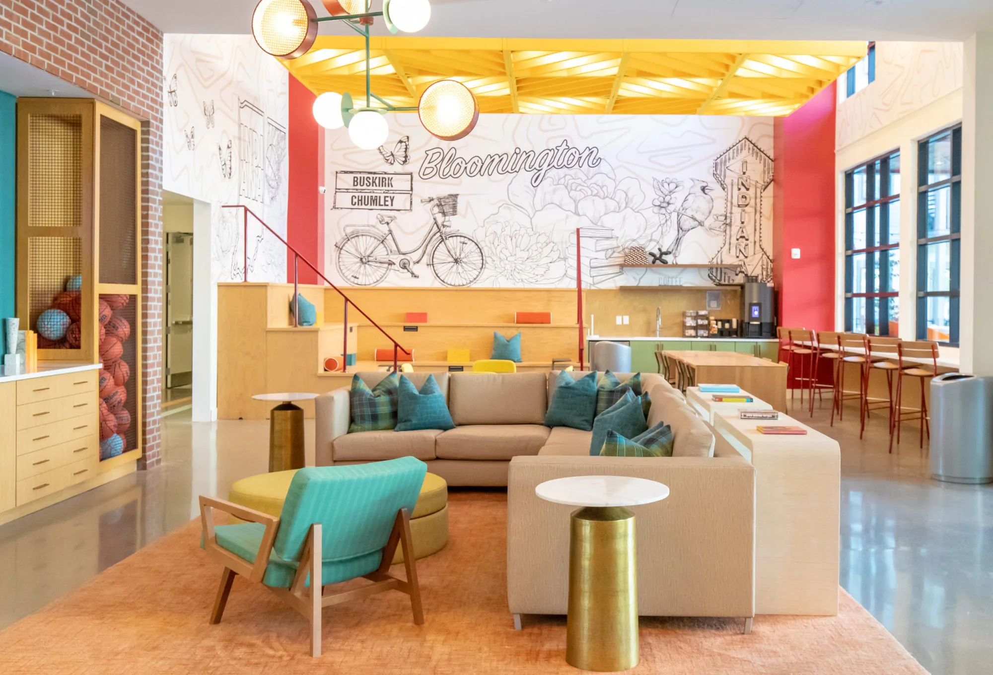 Student housing amenity lobby with a hand-drawn Bloomington mural, a yellow slatted ceiling and a sectional on an orange rug