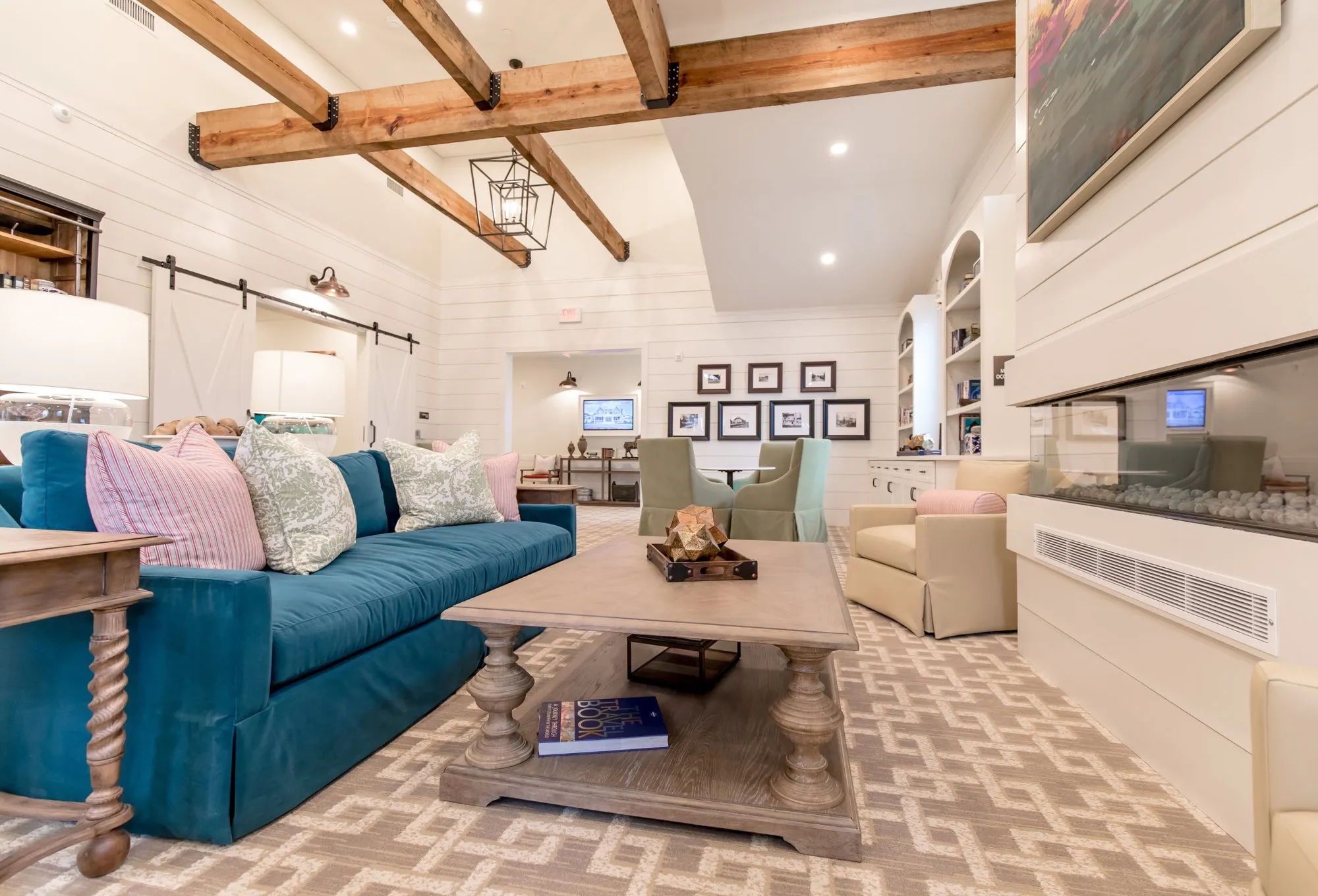 Farmhouse style lounge with exposed beams and shiplap, a teal skirted sofa with pink and sage pillows and a barn door beyond