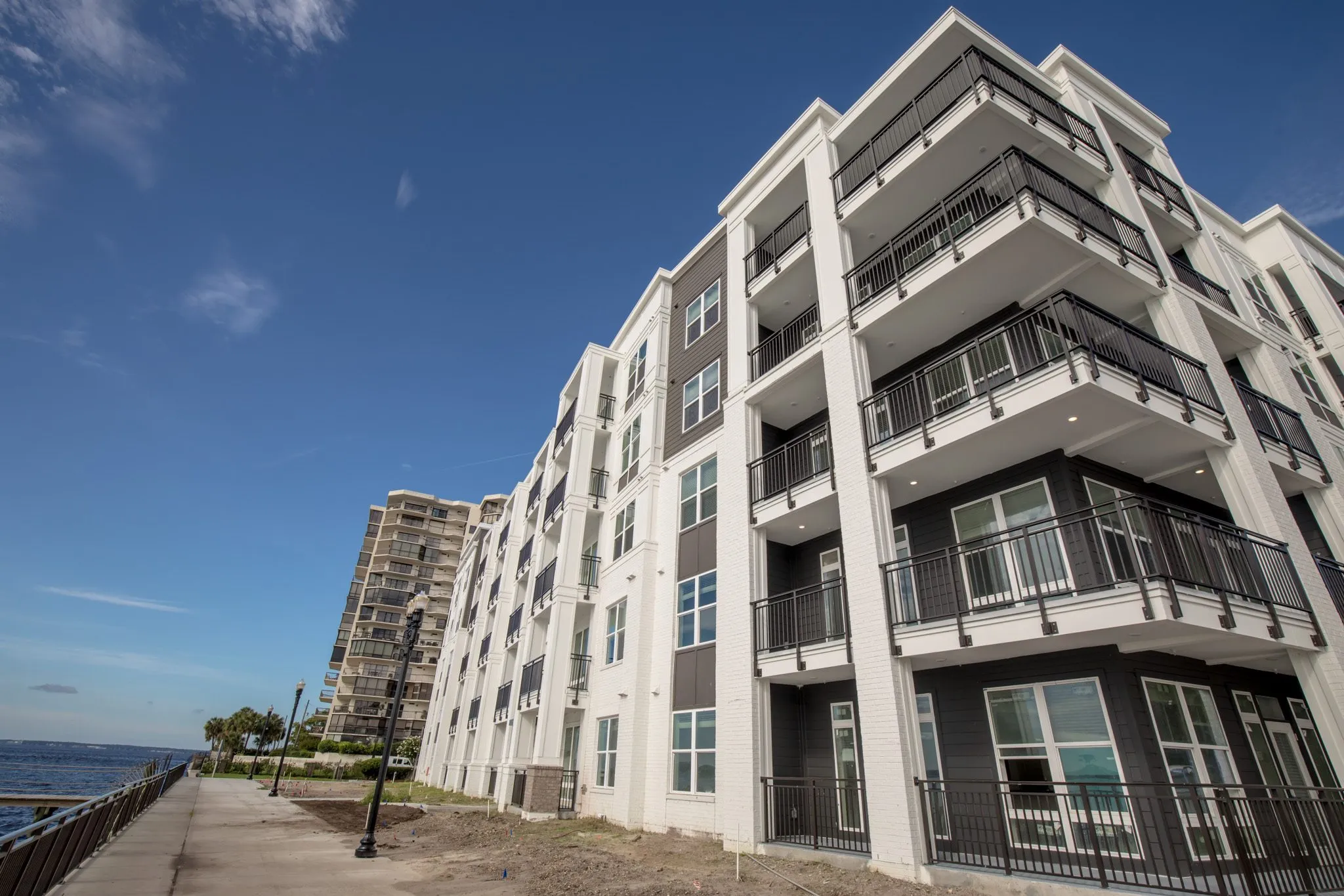 Multifamily community exterior: white residential building with stacked balconies along the riverfront walk