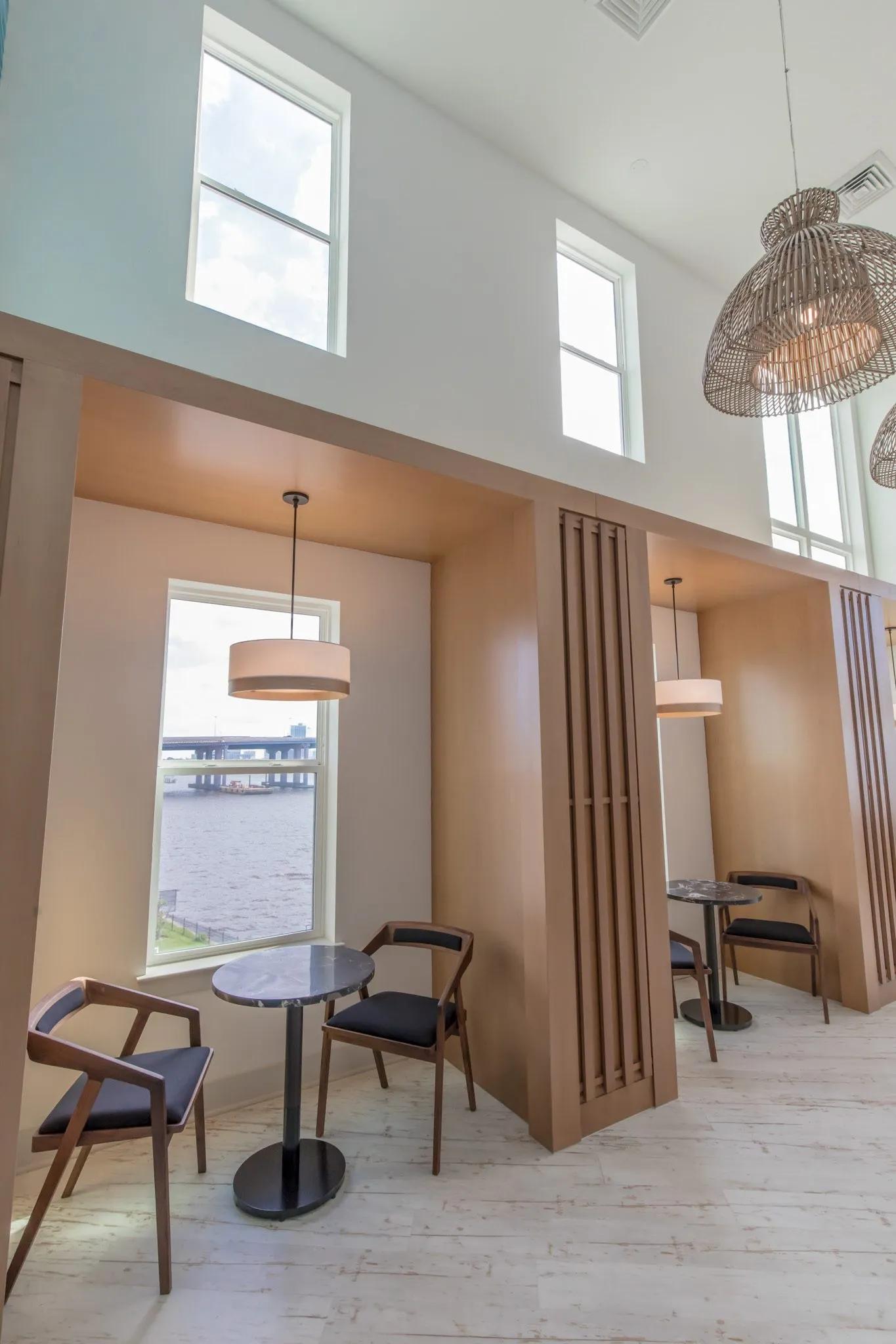 Multifamily amenity work booths with wood surrounds, cafe tables and black chairs below river view windows