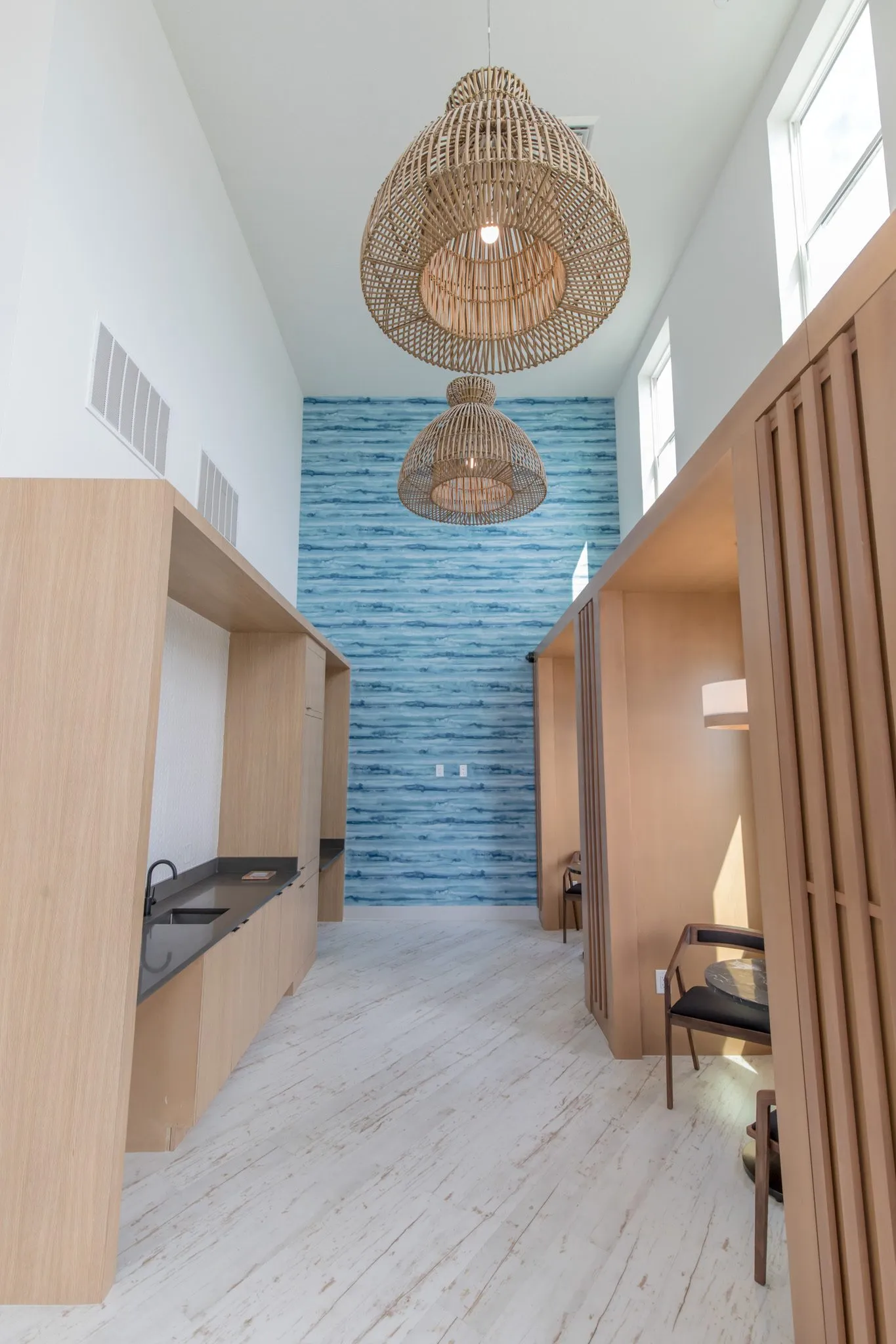 Multifamily amenity corridor of wood booths under woven pendants to a blue water pattern wall, a kitchenette at left