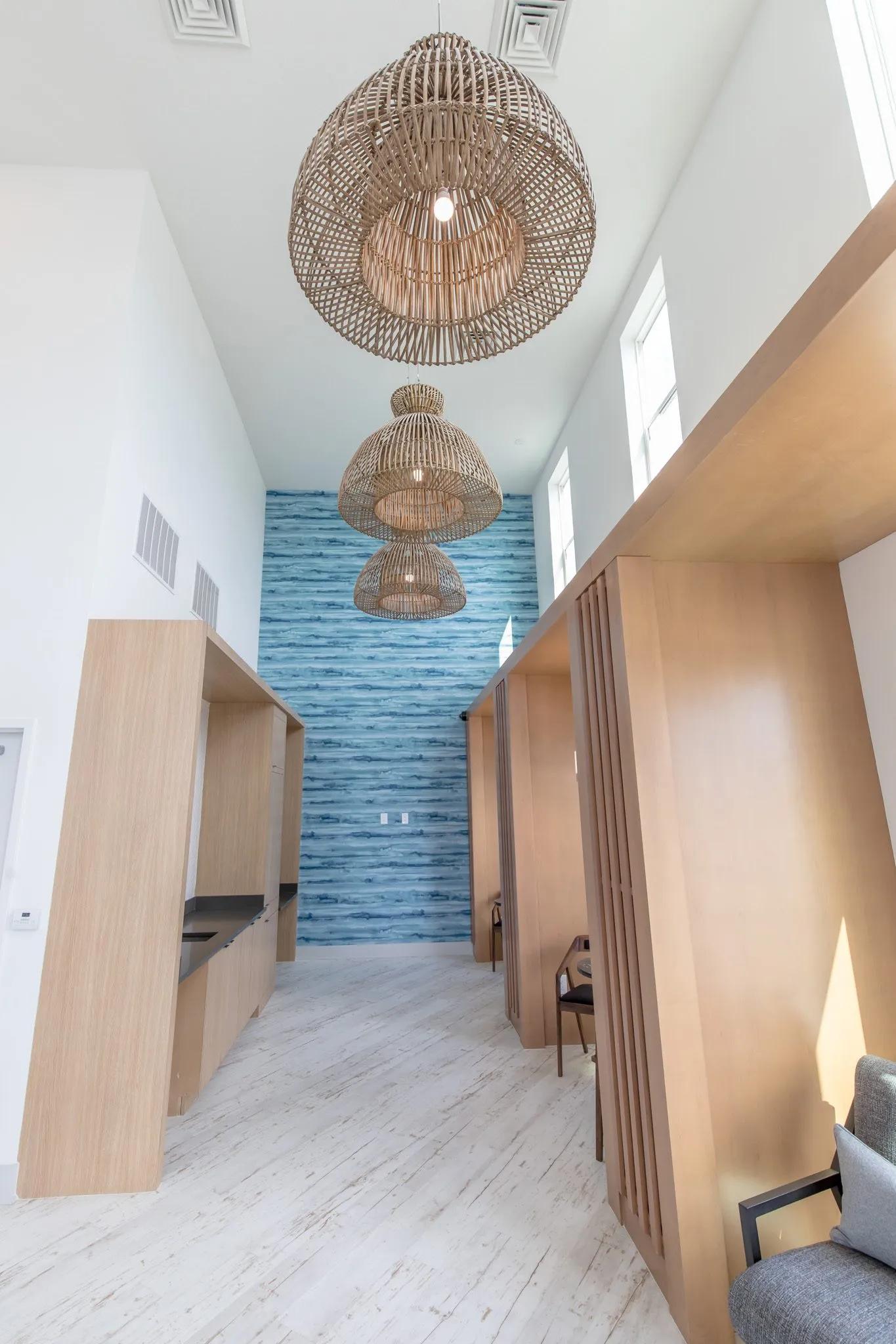 Multifamily amenity booth corridor under three woven pendants to the blue water pattern wall