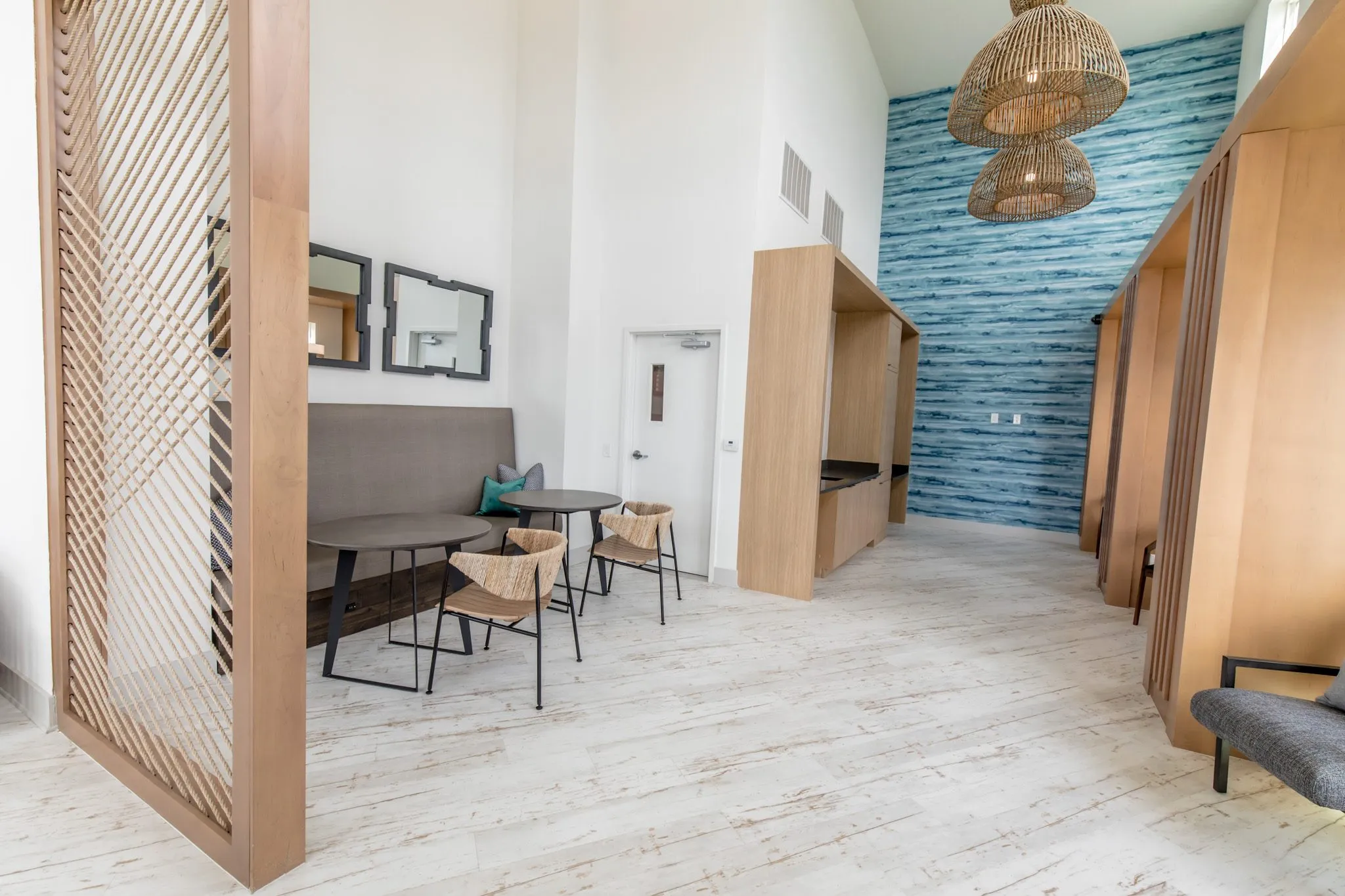 Multifamily amenity clubroom, a banquette with woven chairs at cafe tables by a rope screen, booths and the blue wall beyond