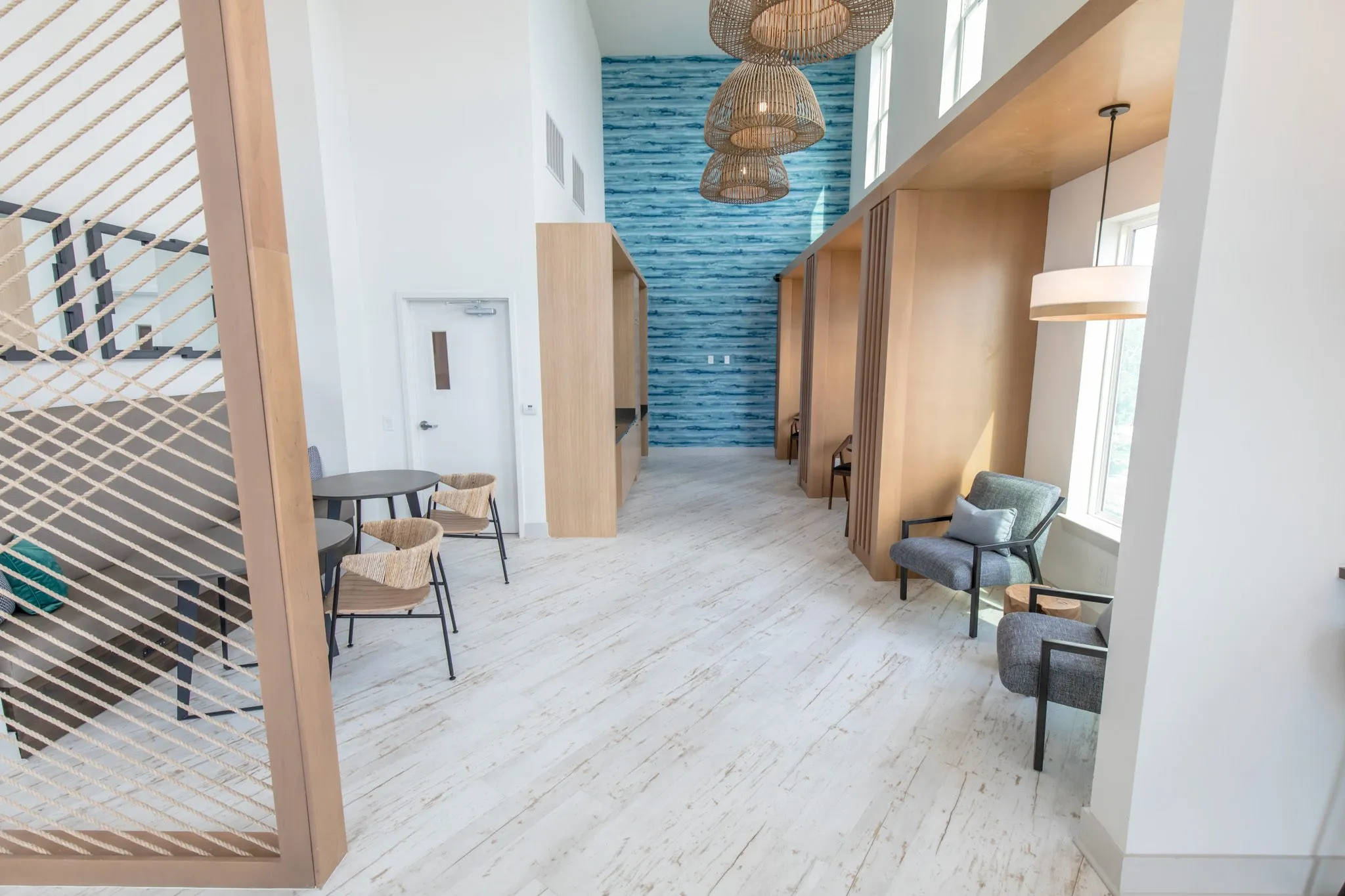 Multifamily amenity booth corridor with grey armchairs by the window and woven chairs at the banquette