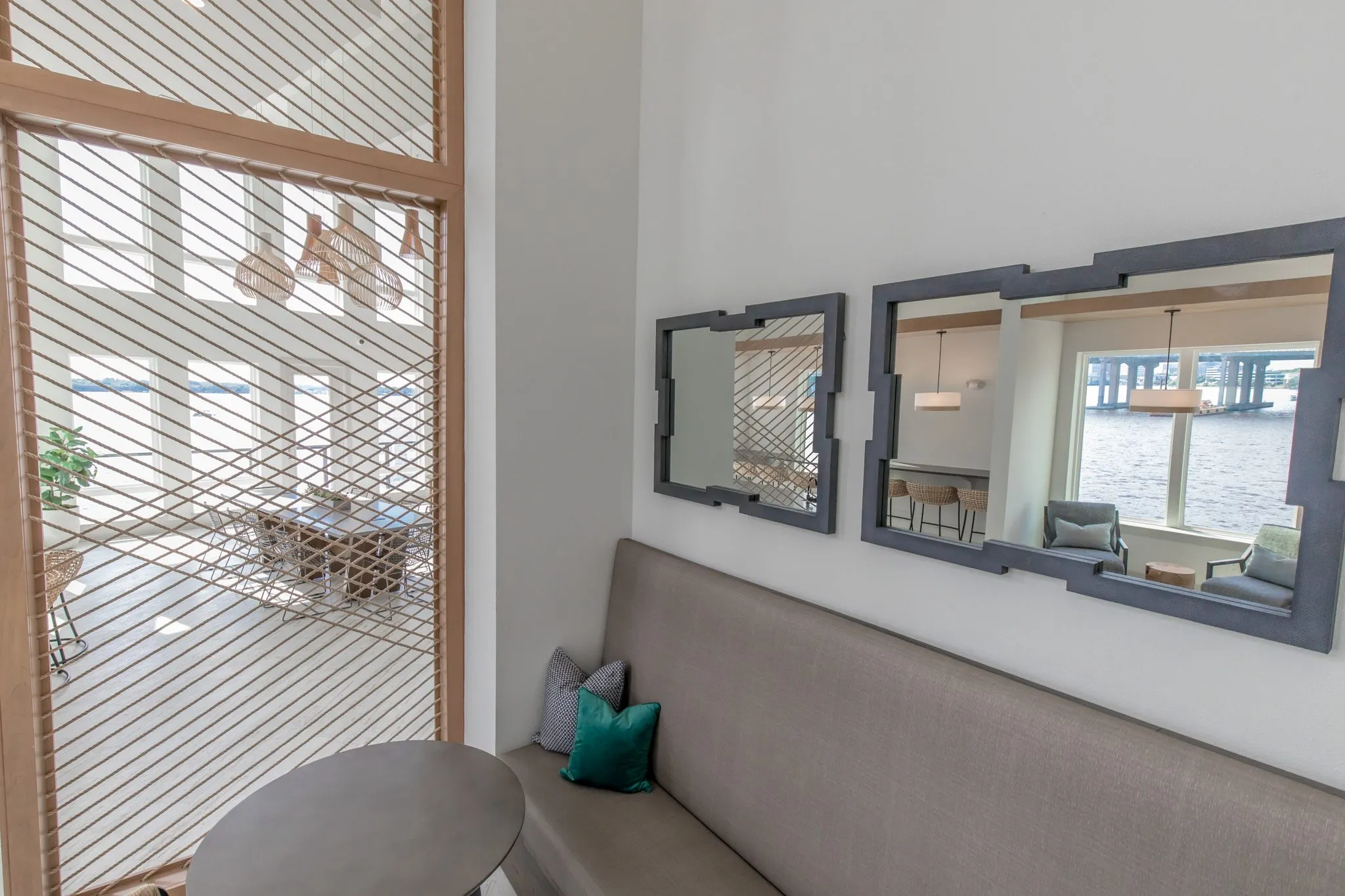 Multifamily interior detail: grey banquette with green and grey pillows under two black framed mirrors beside a rope screen