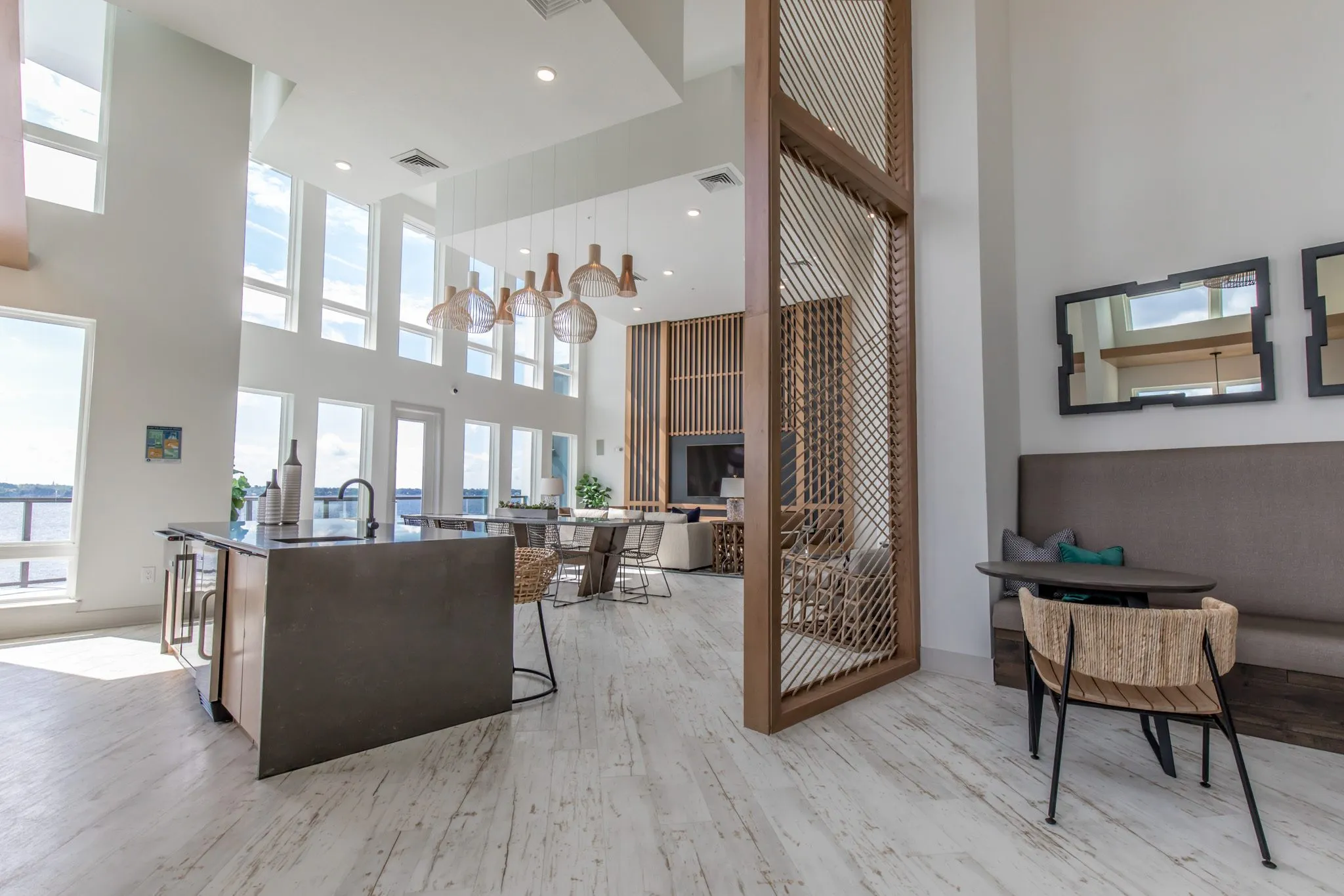 Multifamily amenity clubroom with a kitchen island, dining table under rattan pendants and a rope screen by the banquette