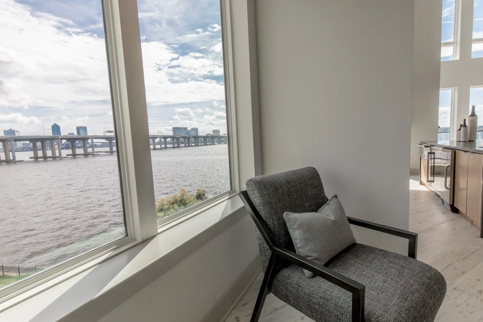 Multifamily interior detail: grey armchair beside a deep window looking over the river to a long bridge and the city