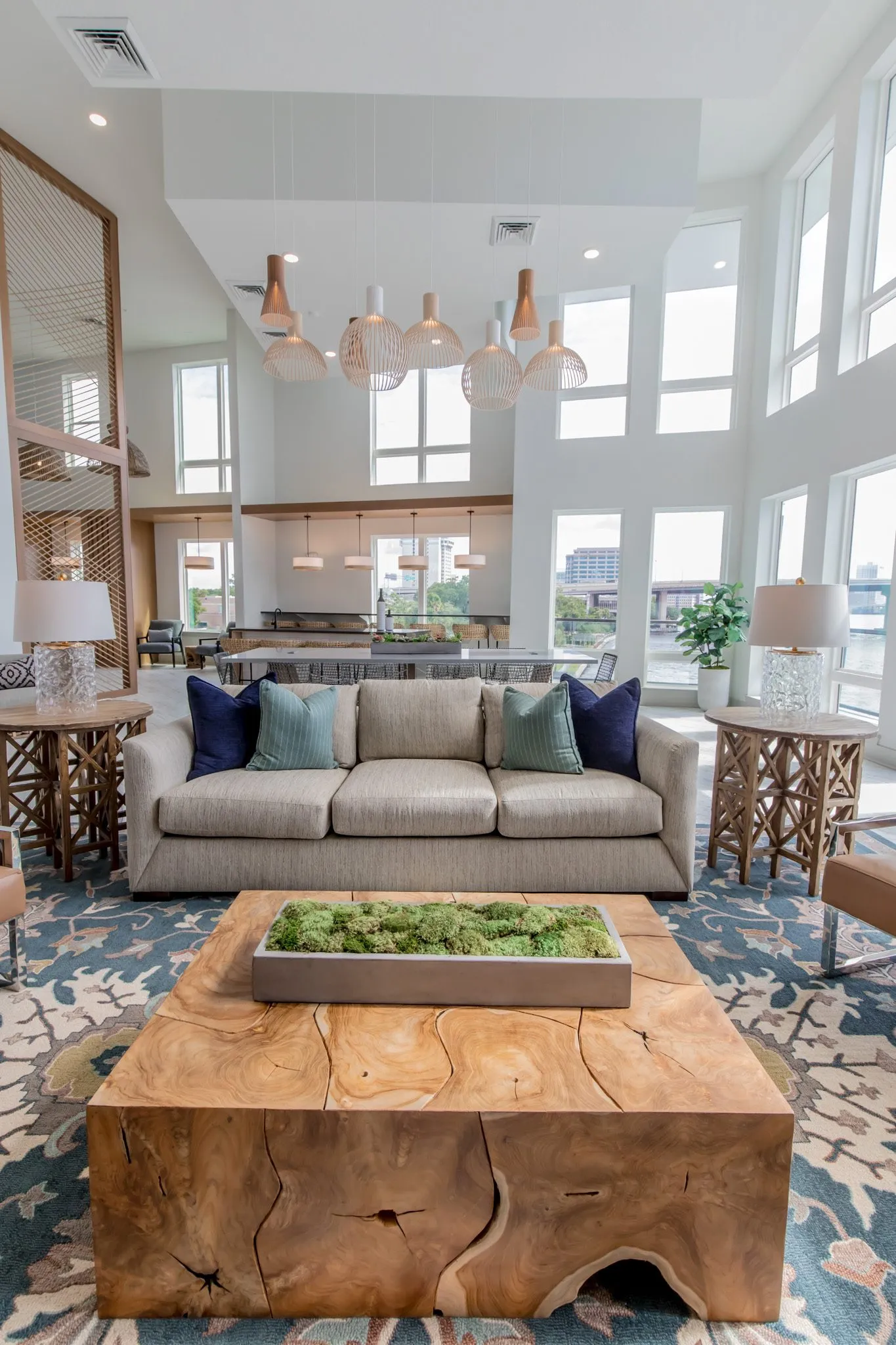 Multifamily amenity clubroom over a timber block coffee table with moss to the sofa, wood pendants and river windows
