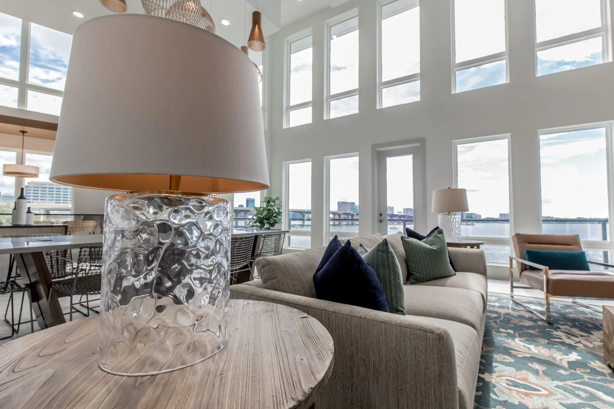 Multifamily interior detail: textured glass lamp on a wood side table, the sofa and river windows beyond