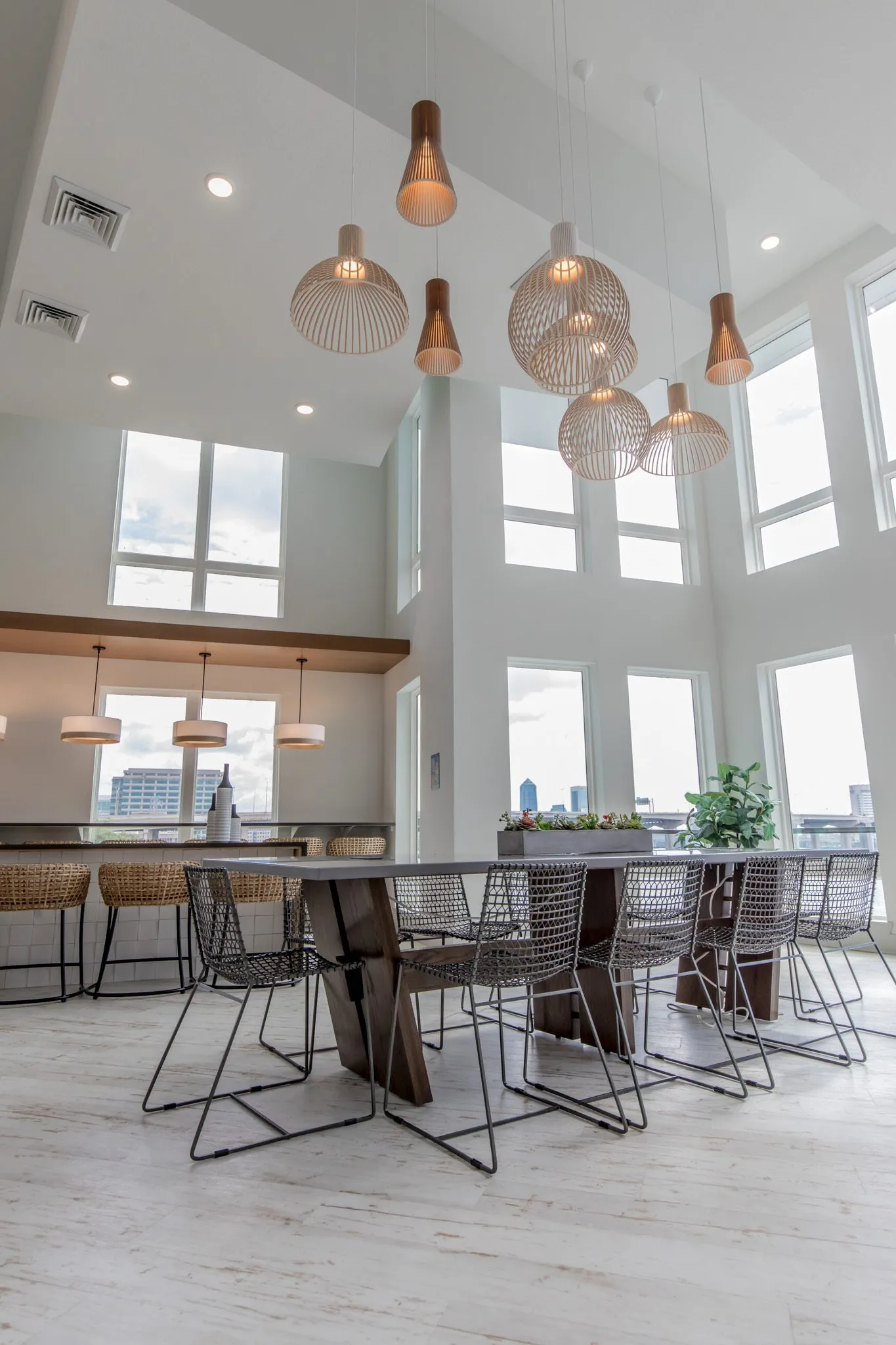 Multifamily amenity clubroom, a low view of the long table with wire chairs beneath clustered wood pendants