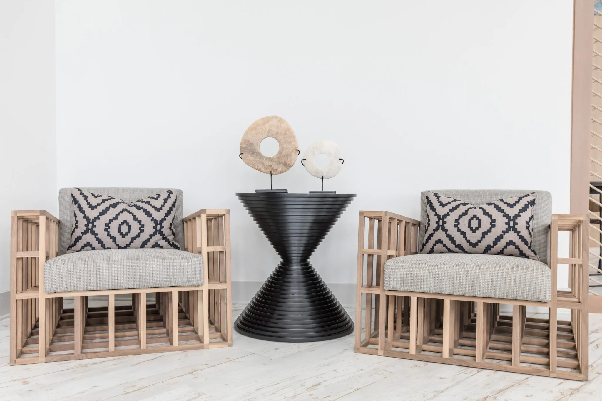 Multifamily interior detail: two slatted wood armchairs with patterned pillows beside a black ribbed hourglass table