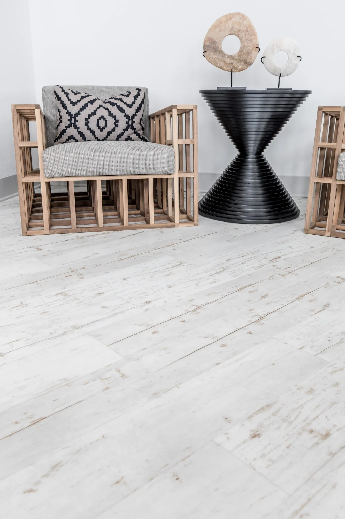 Multifamily interior detail: slatted wood armchair beside a black ribbed hourglass table with stone sculptures