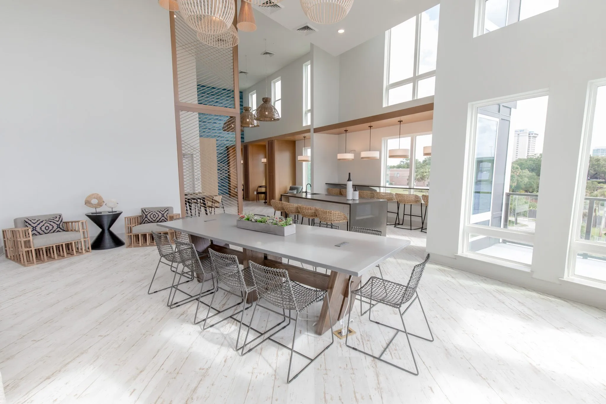 Multifamily amenity clubroom with a long table and wire chairs, the bar, slatted wood armchairs and a blue wall beyond
