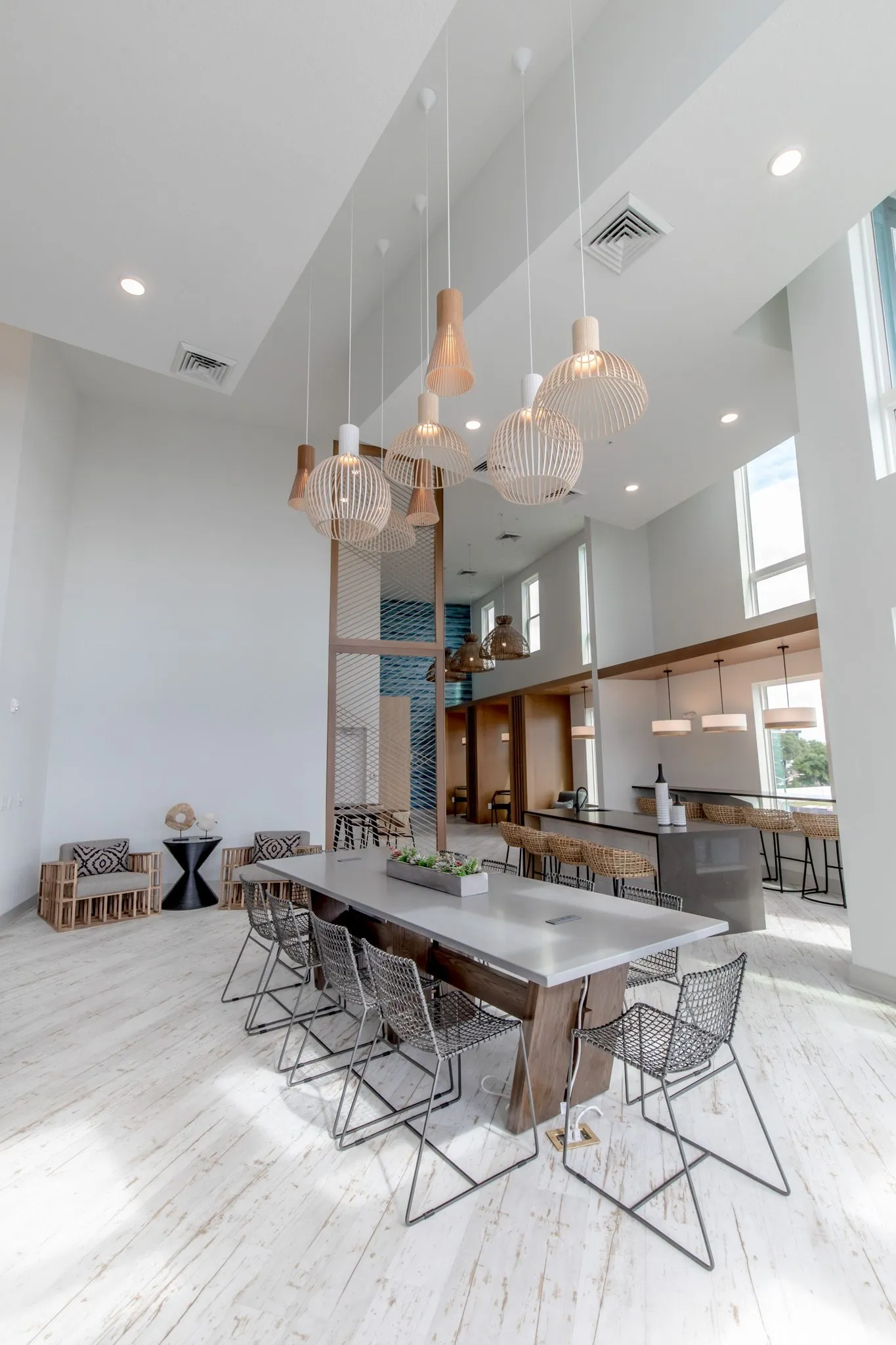 Multifamily amenity clubroom with wood pendants hung over the long table, the bar and slatted armchairs beyond