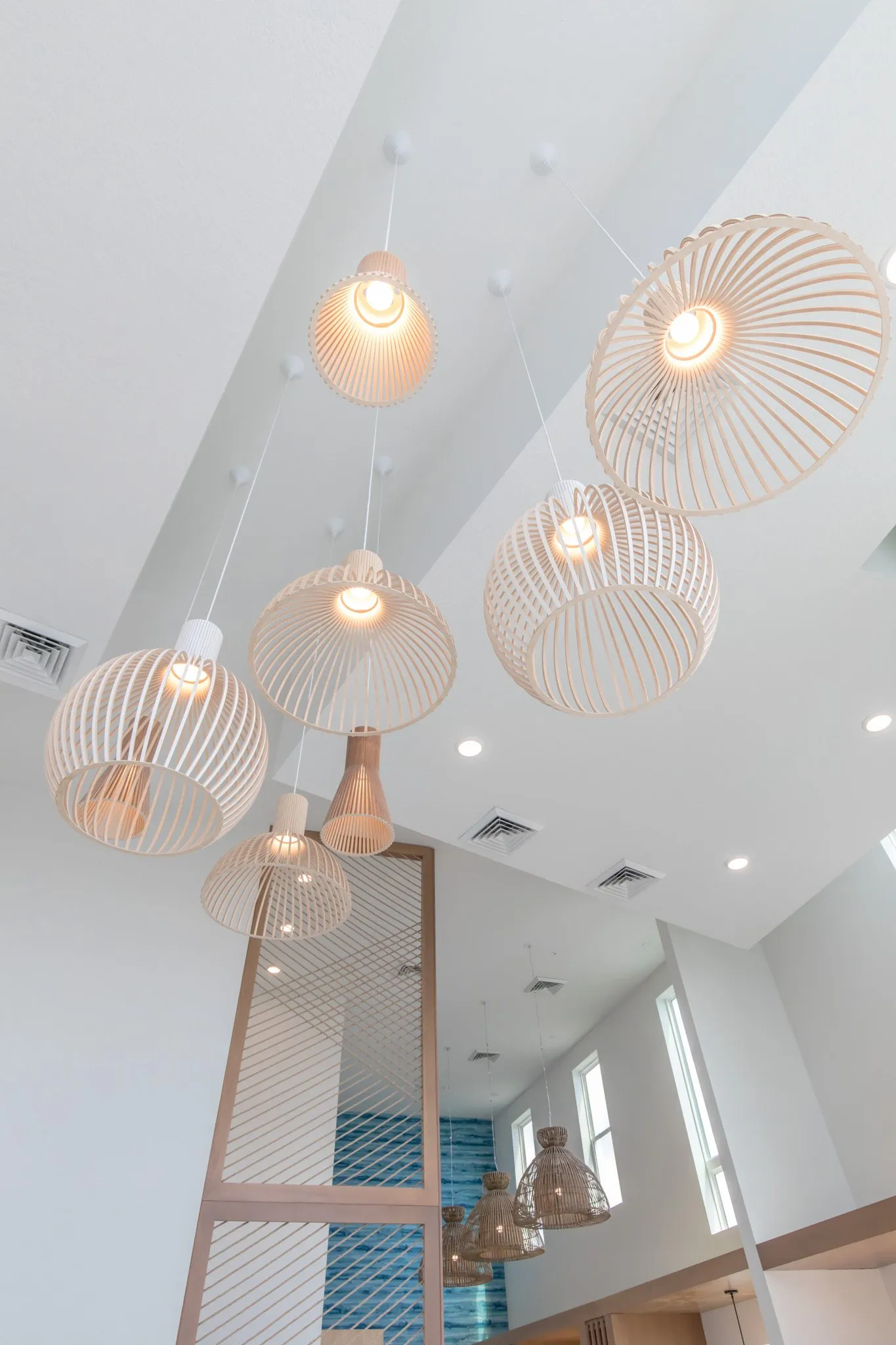 Multifamily interior detail: looking up at clustered pale wood ribbon pendants in the double-height space