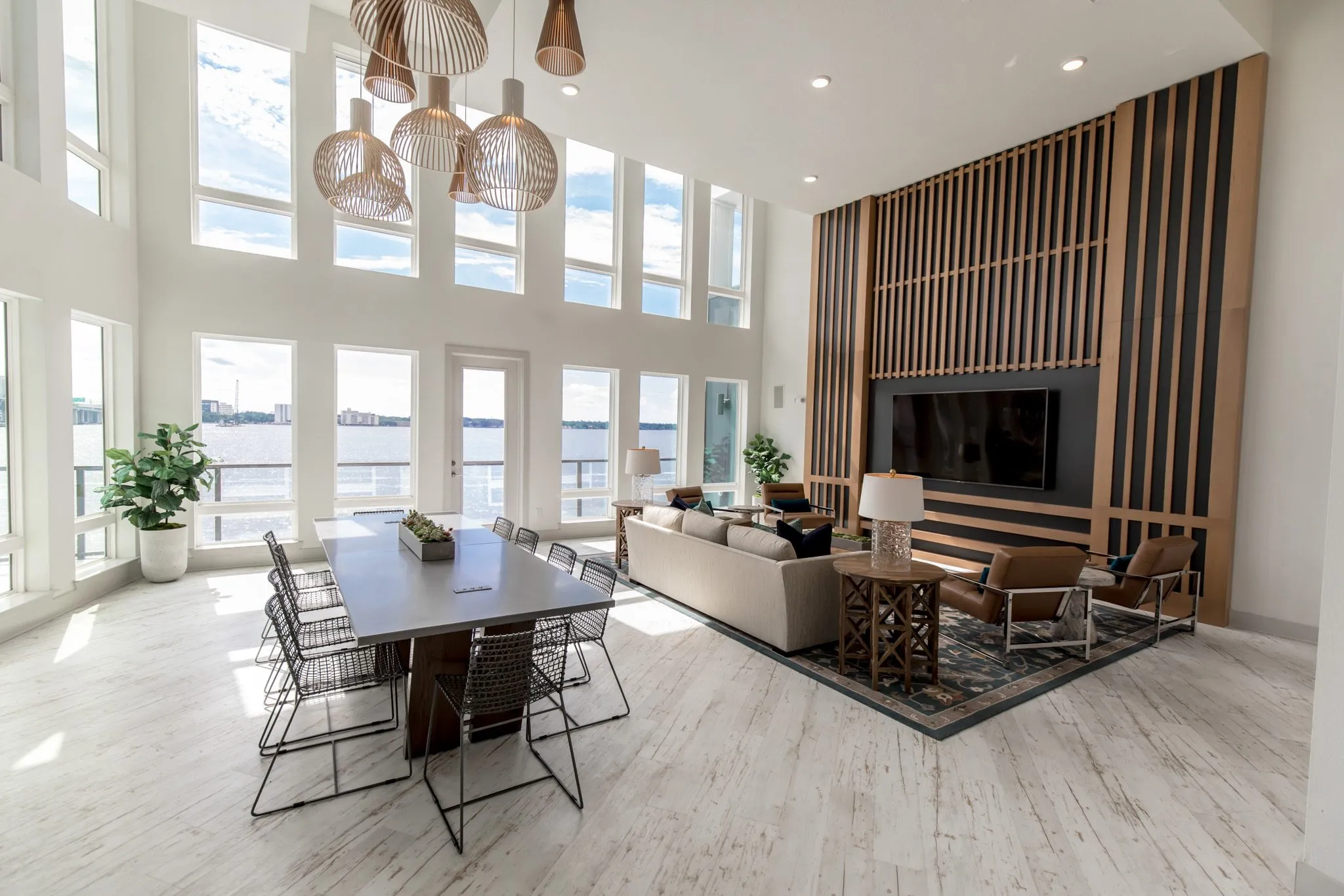 Multifamily amenity clubroom with the long table, sofa and leather chairs facing a wood slat media wall, river windows