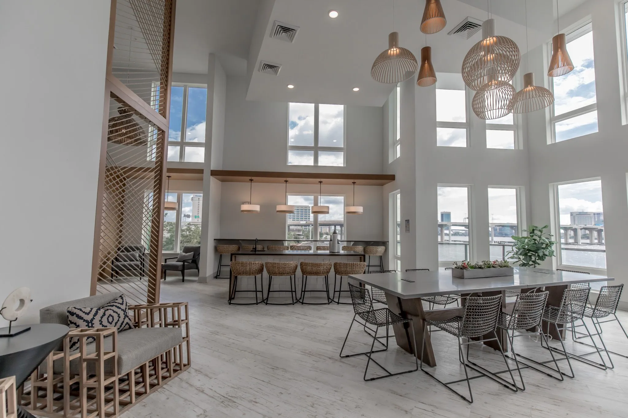 Multifamily amenity clubroom with a slatted armchair, rope screen, island with stools and long table under wood pendants