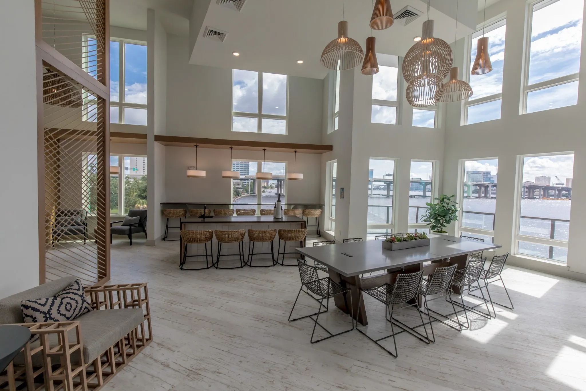 Multifamily amenity clubroom with a slatted armchair at left, island stools and long table under wood pendants